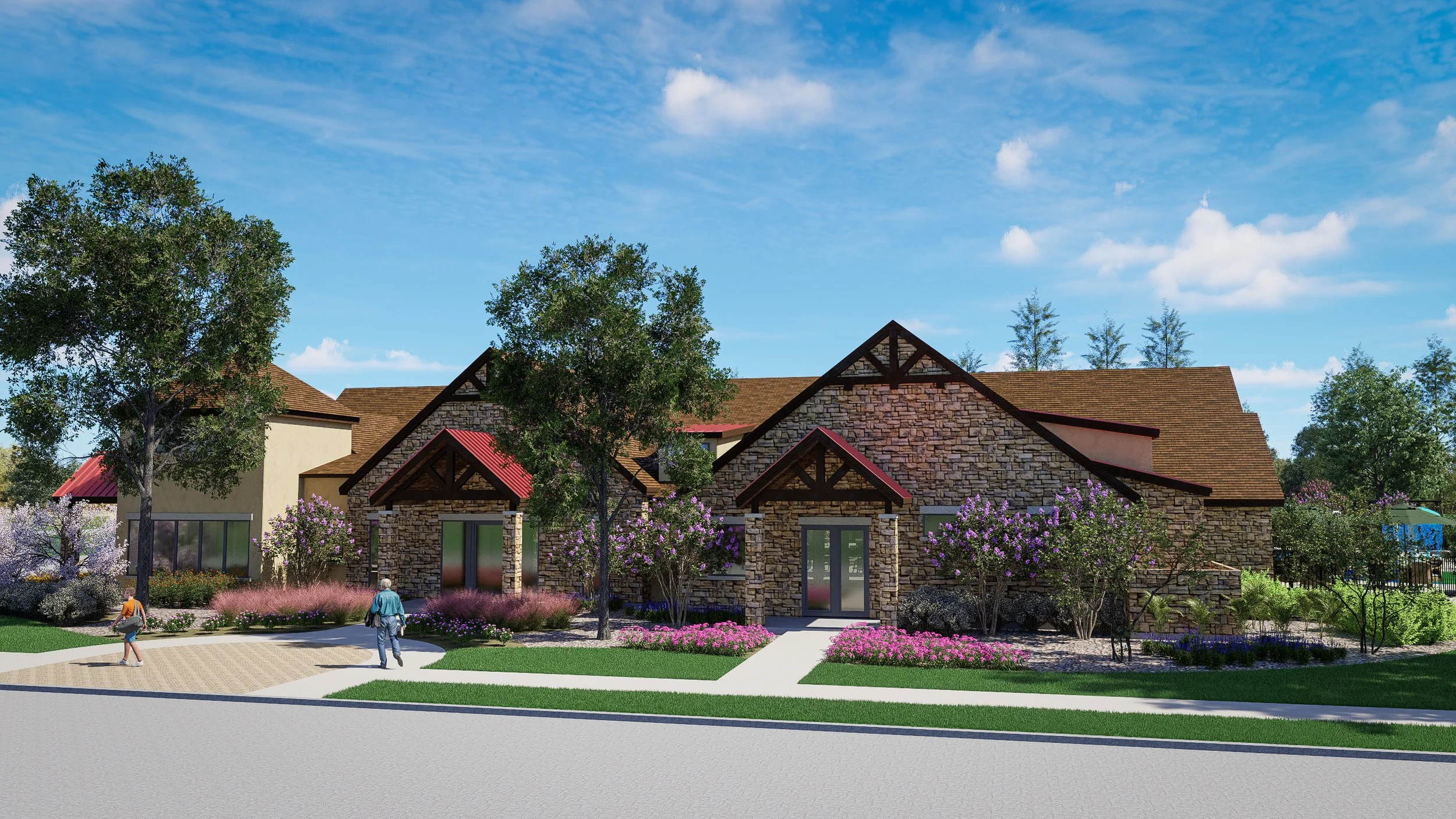 A modern residential building with stone and stucco exterior, surrounded by landscaped gardens, flowering bushes, and mature trees, under a partly cloudy blue sky.
