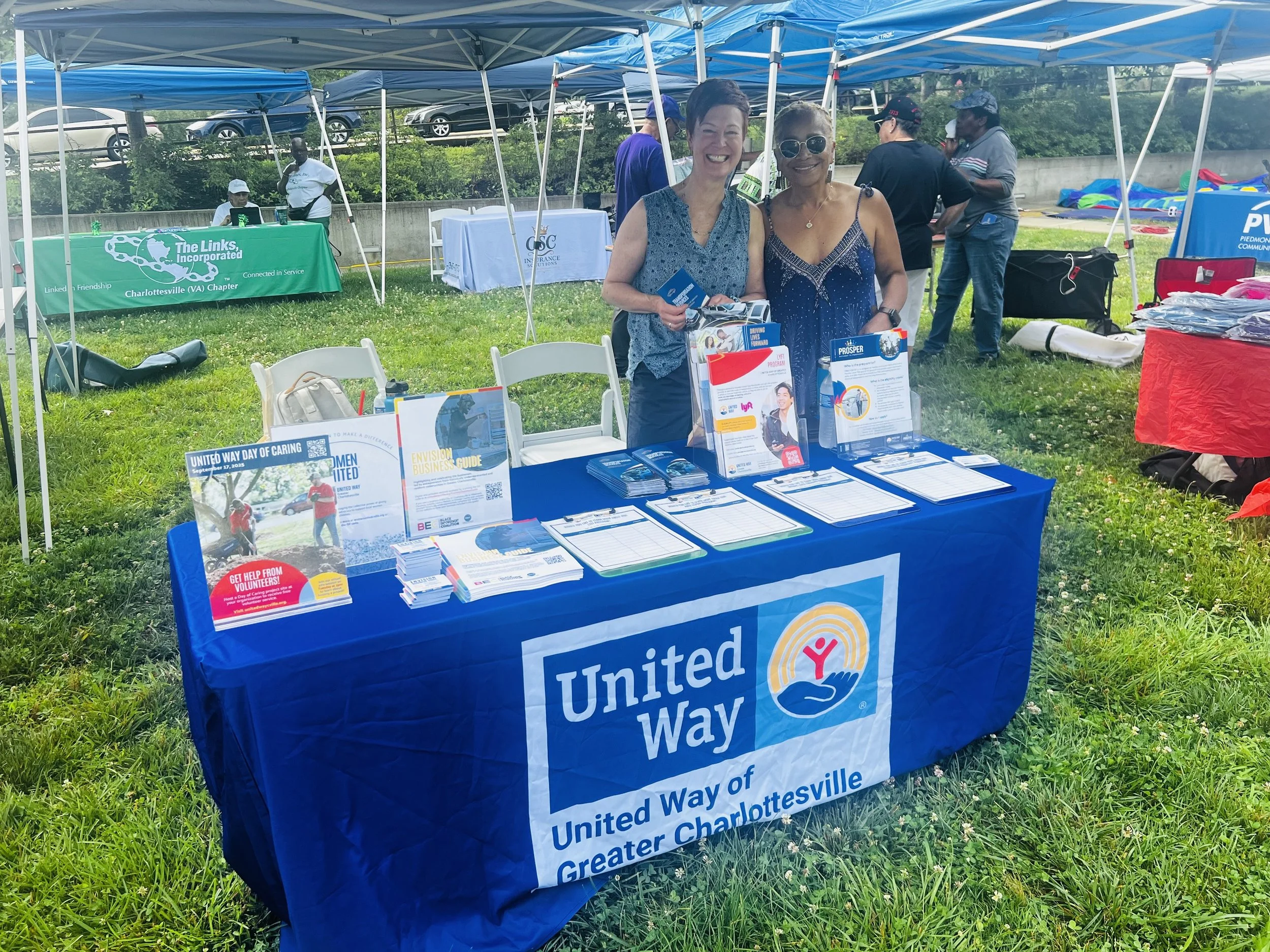 Two women standing behind a United Way promotional table outside, with tents and other booths in the background.