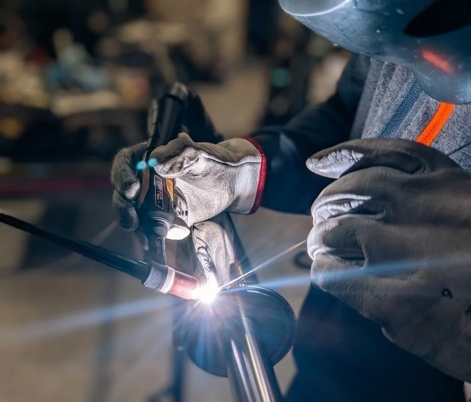 Un fabbro indossa guanti e casco mentre utilizza una pinzatrice per saldare un componente metallico.