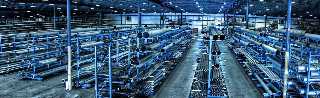 Interno di un magazzino di metalli con scaffalature blu e tubi metallici di varie lunghezze e diametri.
