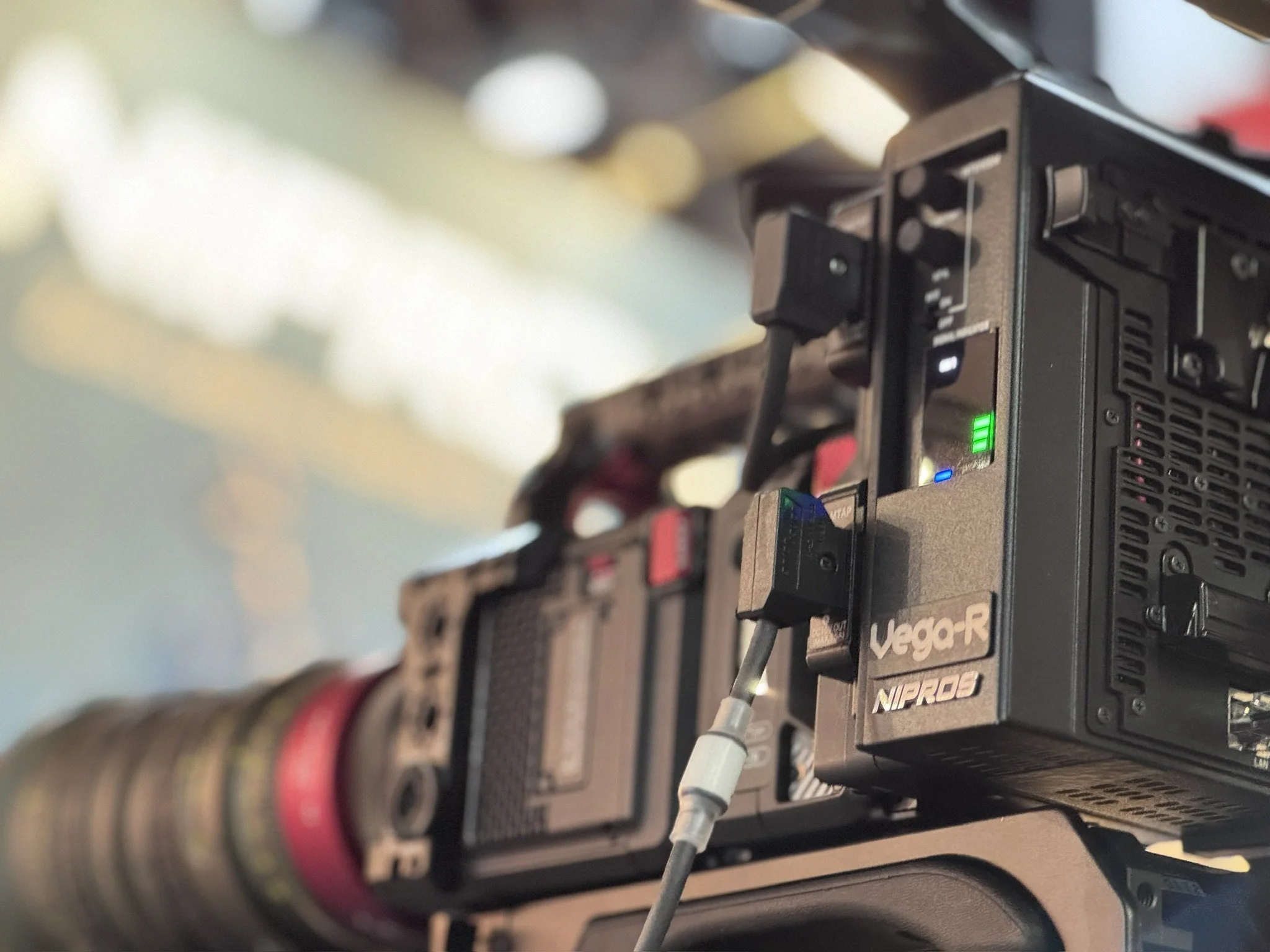 Close-up of a professional video camera with various controls and colorful cables connected, capturing footage in a studio or production environment.