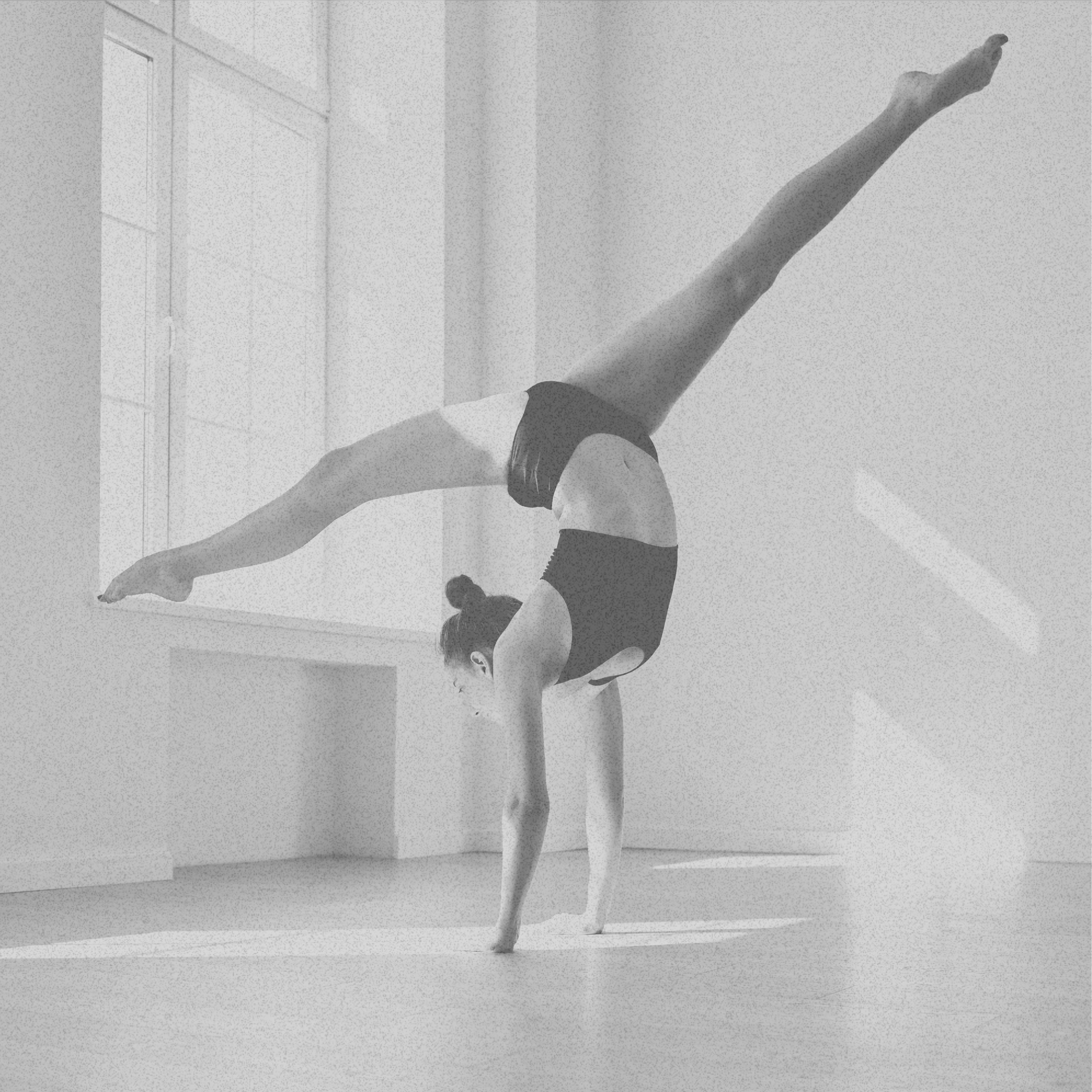 A girl performing a handstand split pose in a studio with large windows and natural light.