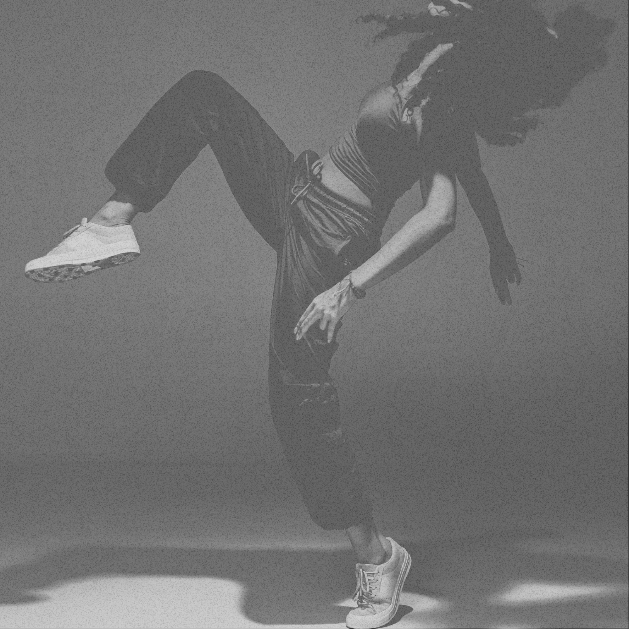 Woman with long hair and sneakers performing a hip hop move against a plain background.