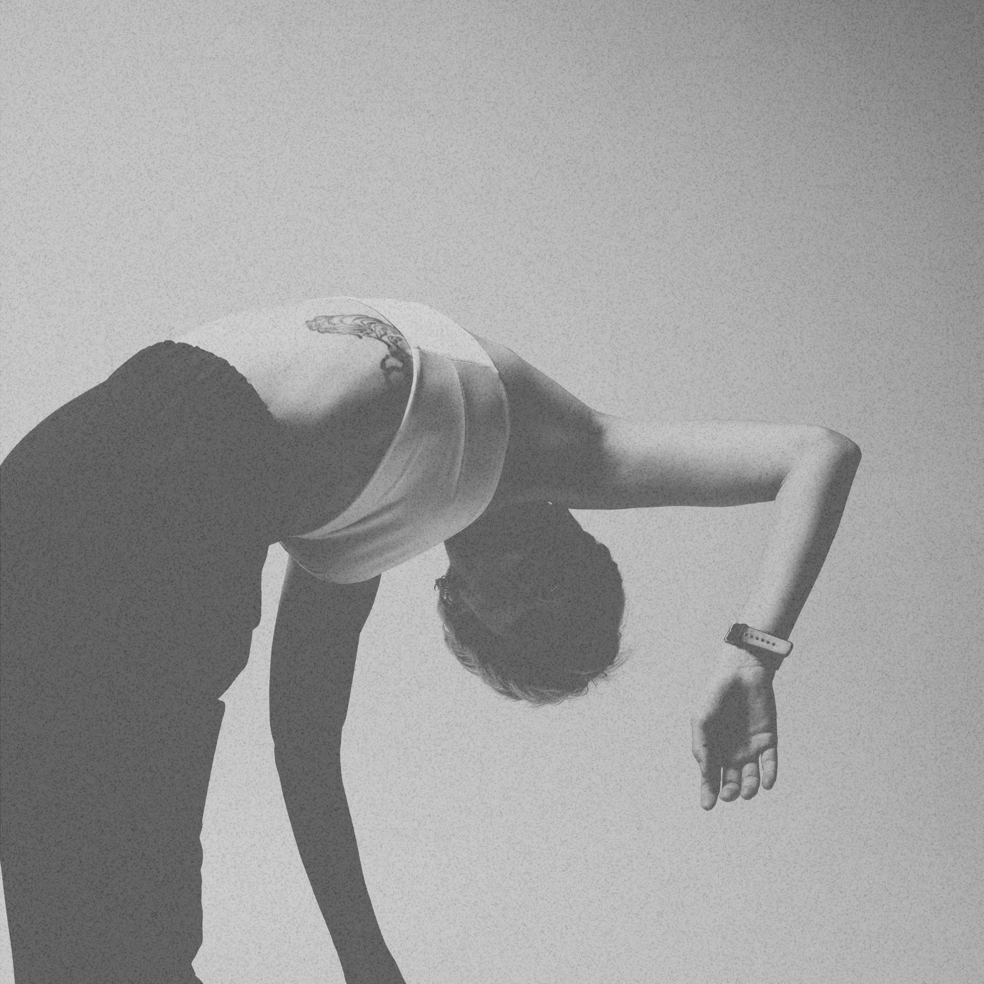 A person is bent over at the waist with their head facing downward and their right arm hanging. They are wearing a wristwatch on their right wrist a white top with black pants. Face is obscured by shadow.