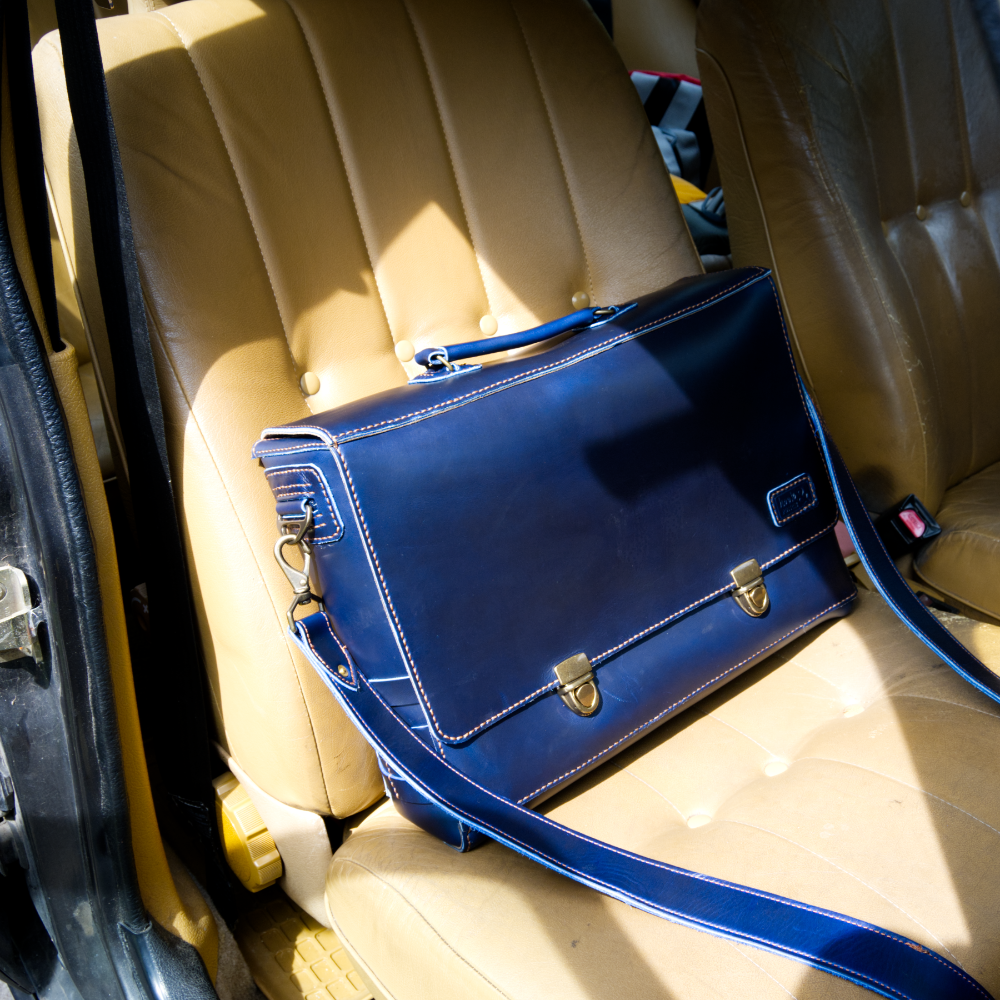 Dark blue leather satchel bag on beige car seat.