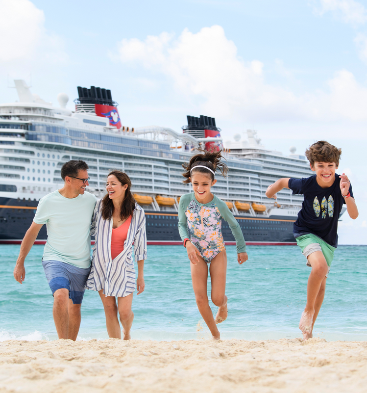 A family of four enjoying time on the beach near the Disney Wish cruise ship, with the parents and children smiling and running on the sand.