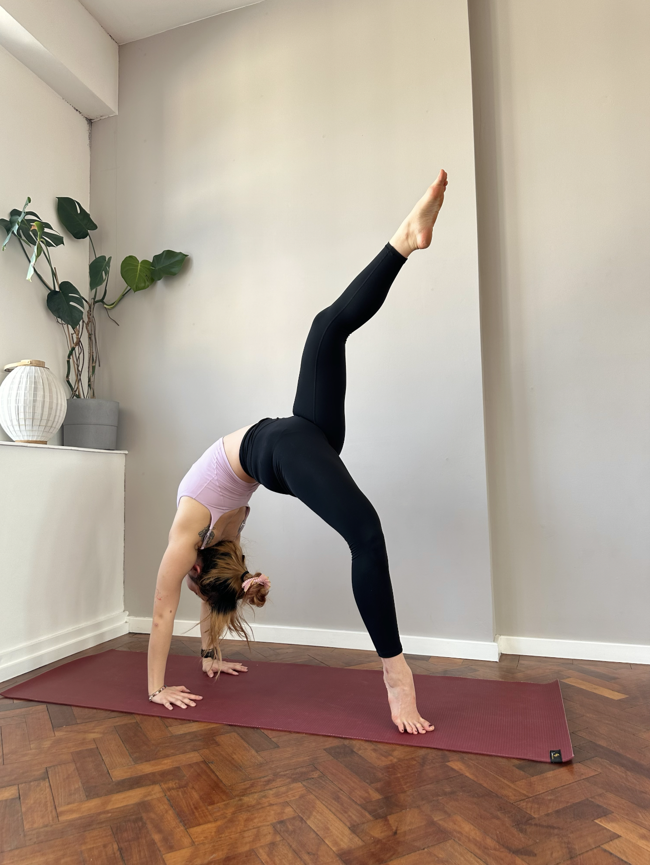 A woman practicing yoga in downward dog pose in a room with hardwood floors and minimal decor.