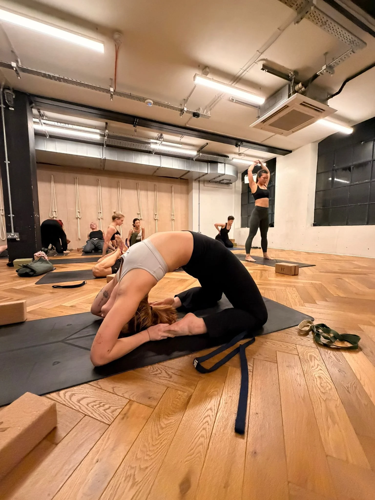 A woman practicing yoga in a studio with others in the background.