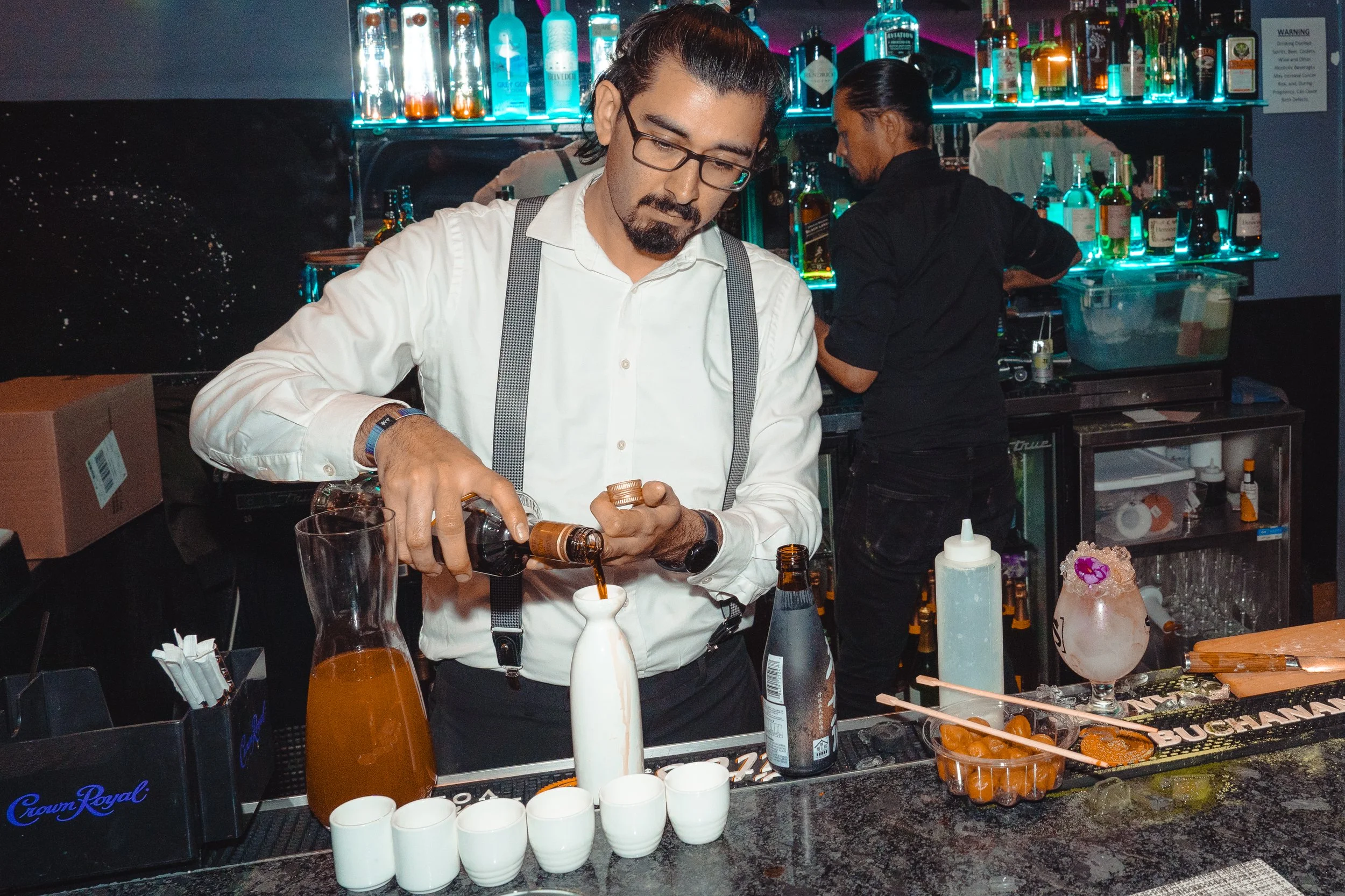 Pura Buddah private event bartender pouring alcohol into drinkware for guests. Cocktails and garnishes can be seen