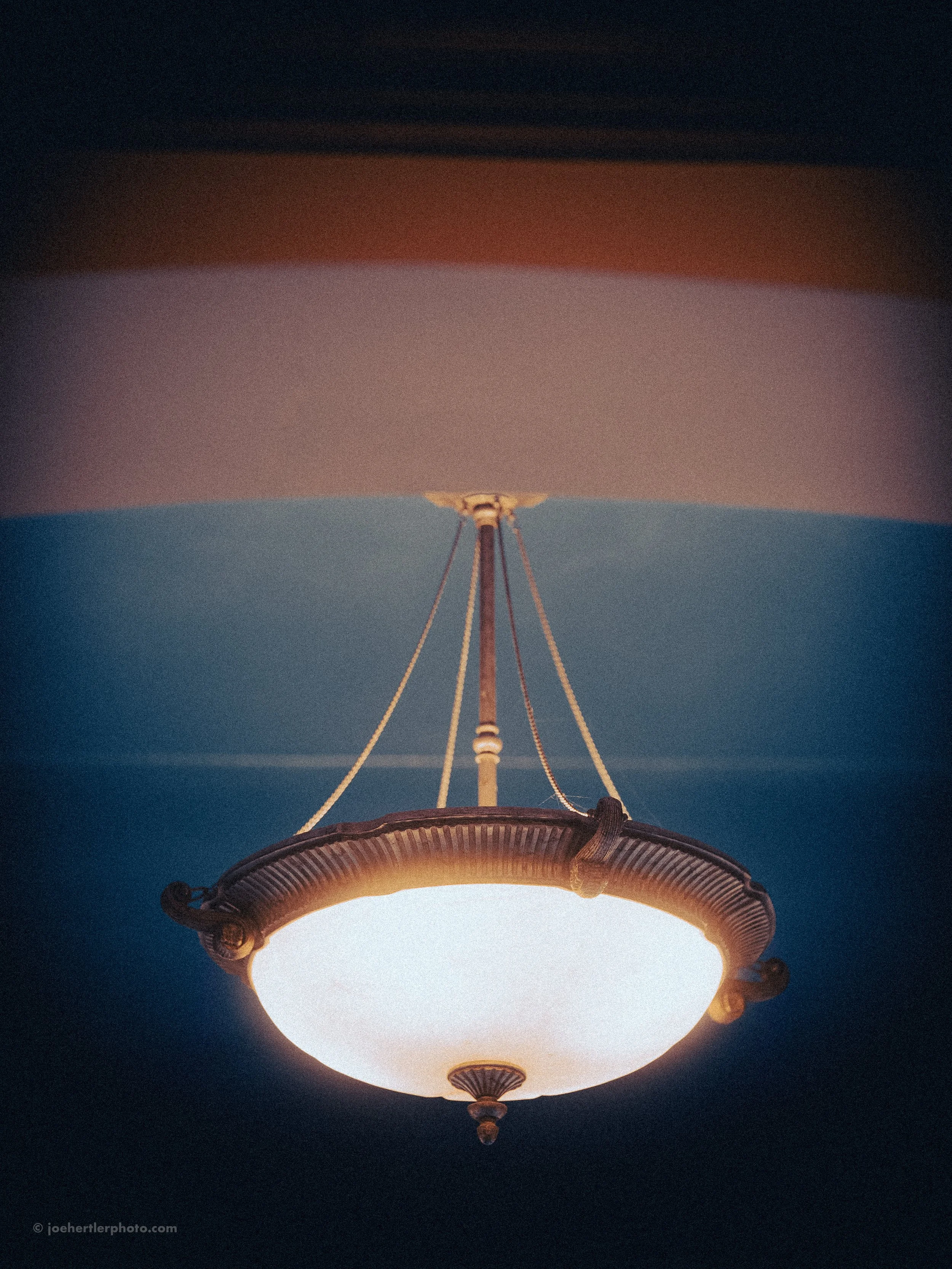 Close-up of a vintage hanging ceiling light fixture with a white frosted glass shade, suspended from the ceiling with metal chains