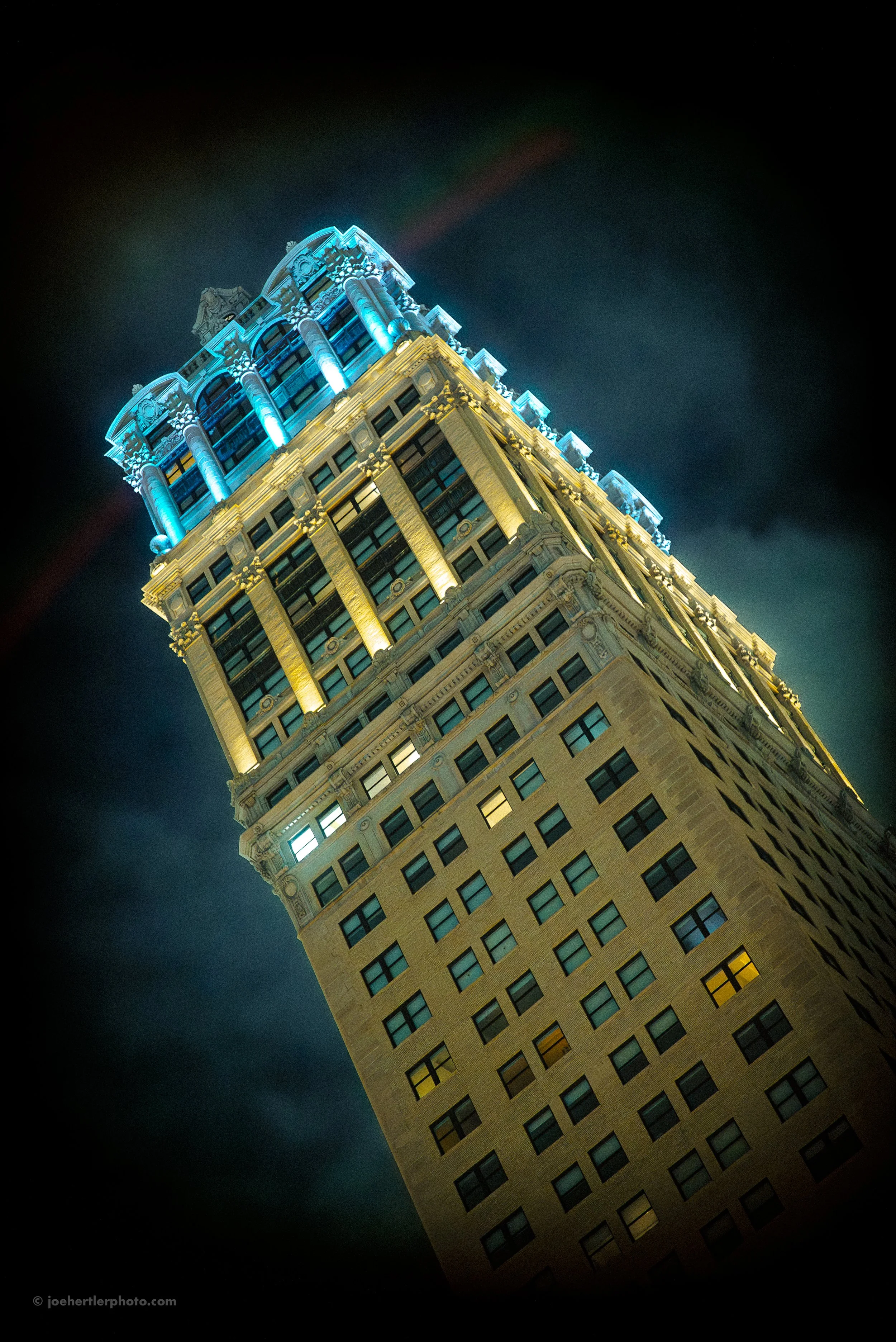 A tall, illuminated building at night with decorative architectural features and a light display at the top.