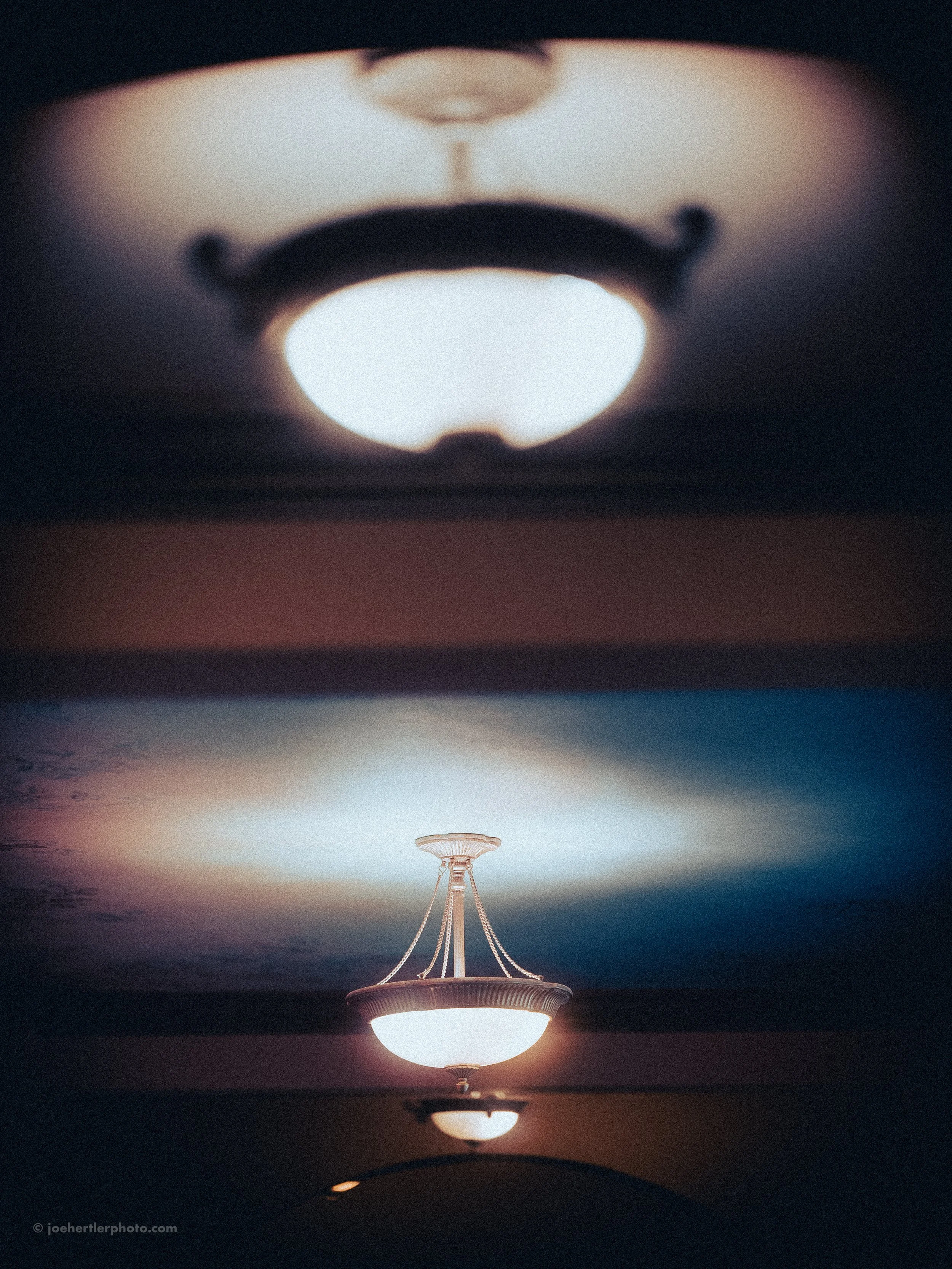 Ceiling light fixture with semicircular shade, reflected on a glossy ceiling, creating a symmetrical mirror image.