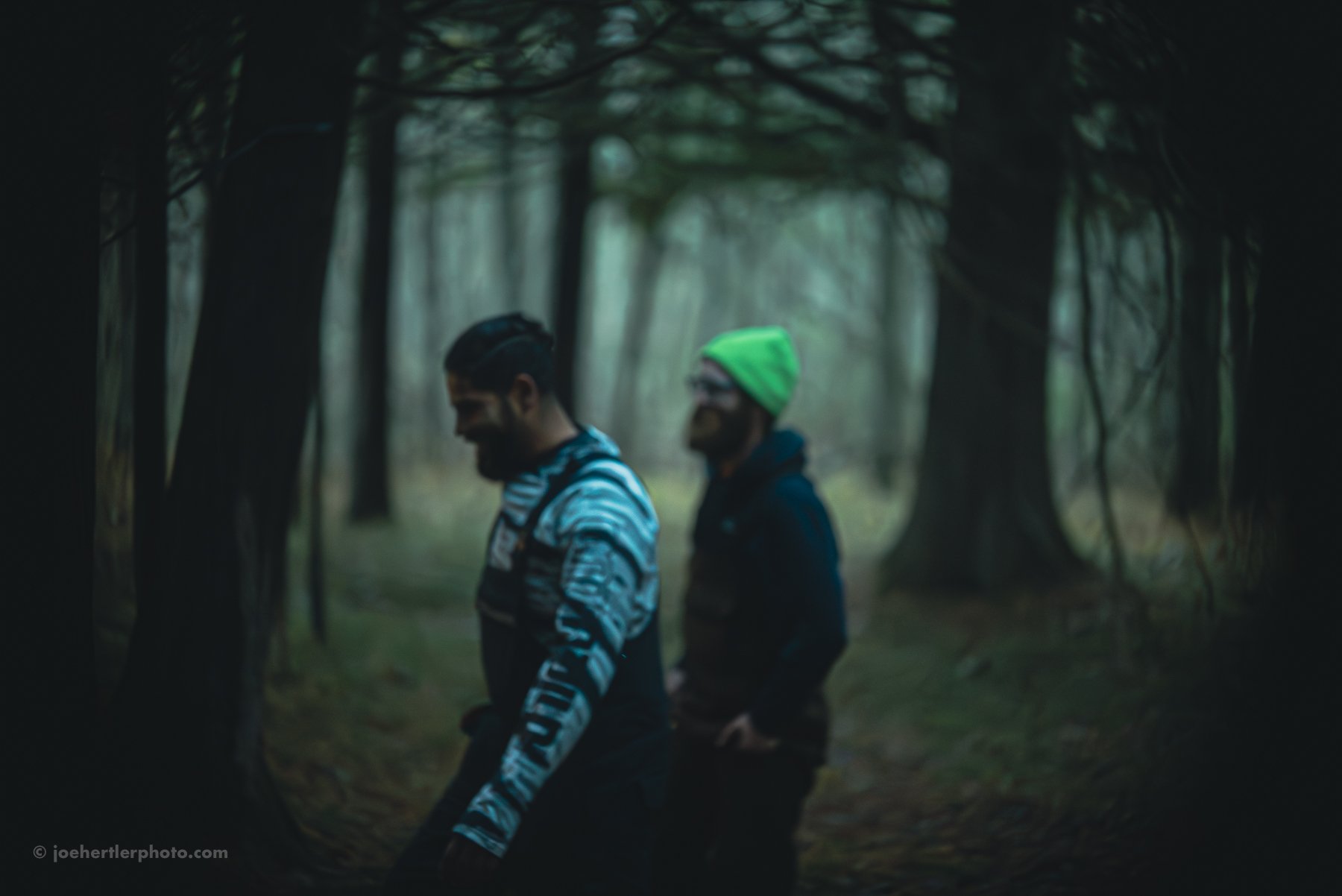Two men walking through a foggy forest, one wearing a striped blue hoodie and the other a black jacket with a neon green beanie.