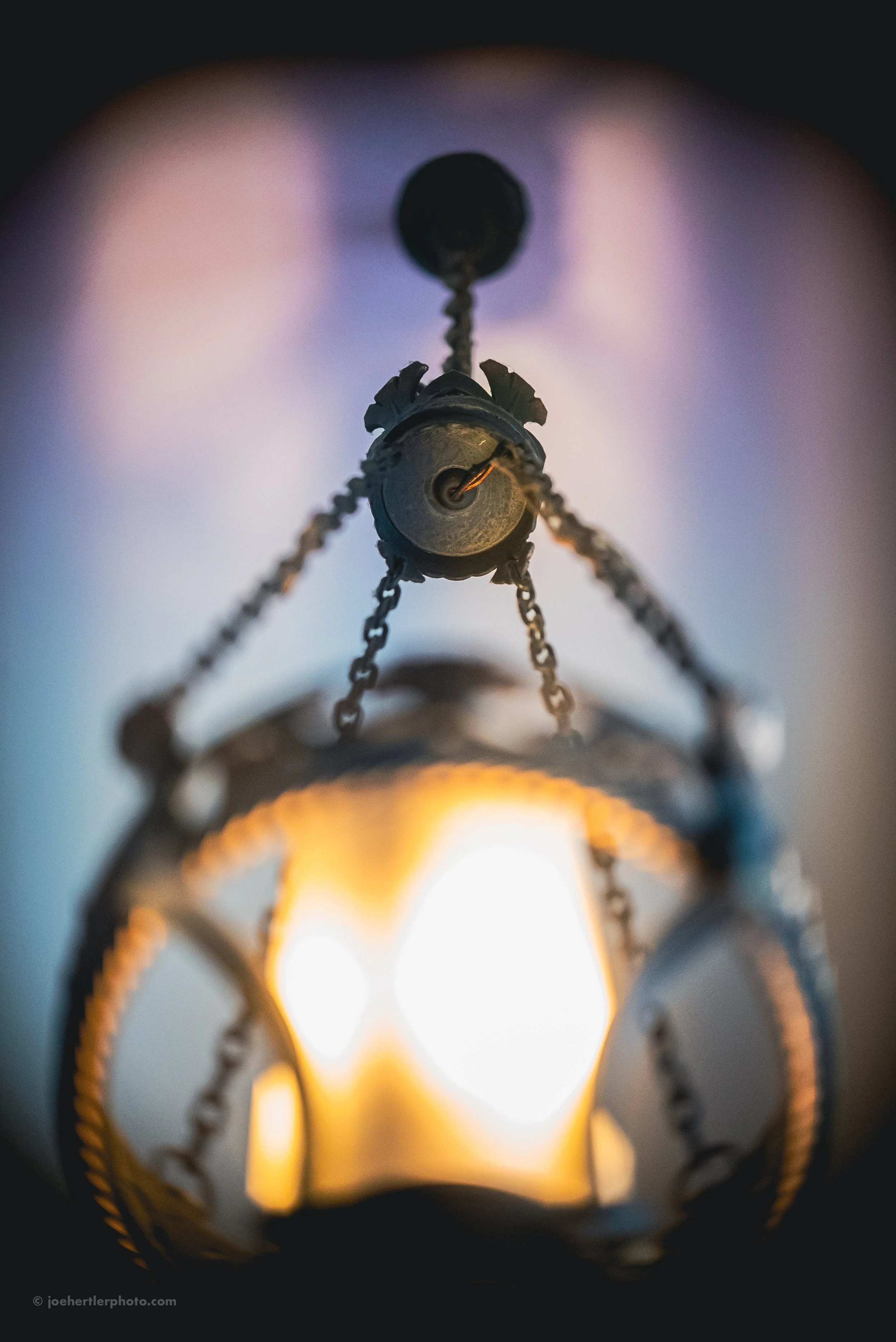 Close-up of a vintage hanging chandelier with ornate metal decoration and a warm glowing light bulb.