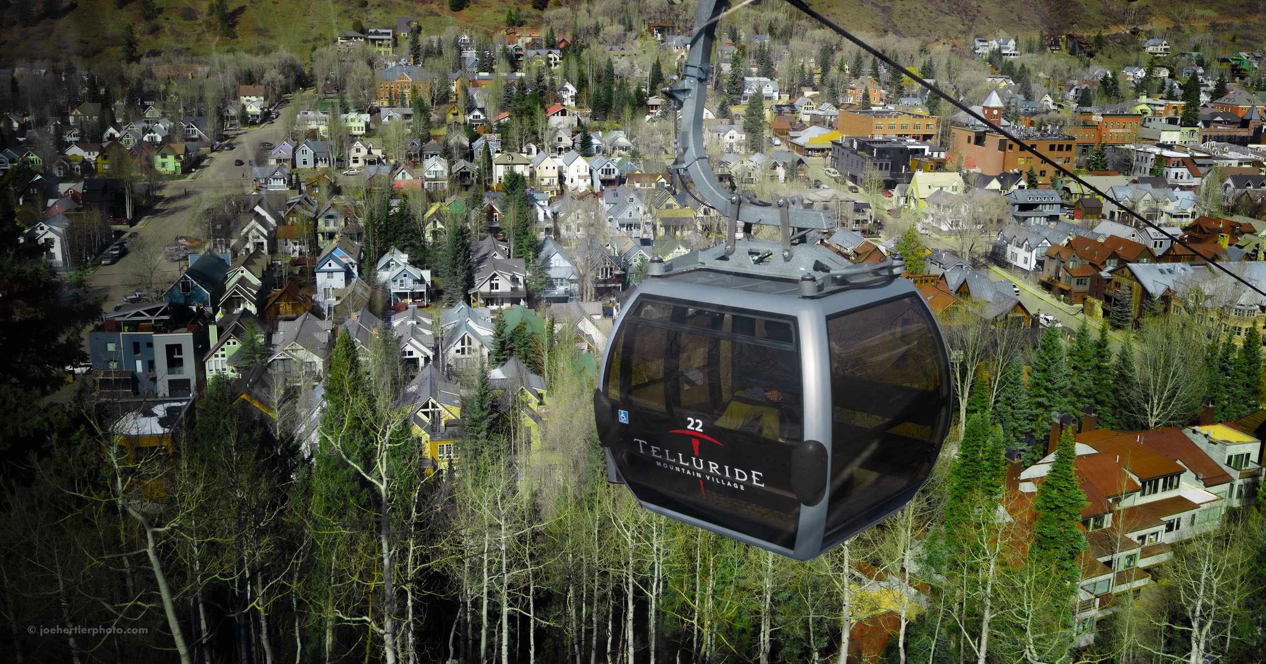 A gondola lift moving over a small town with colorful houses and trees.