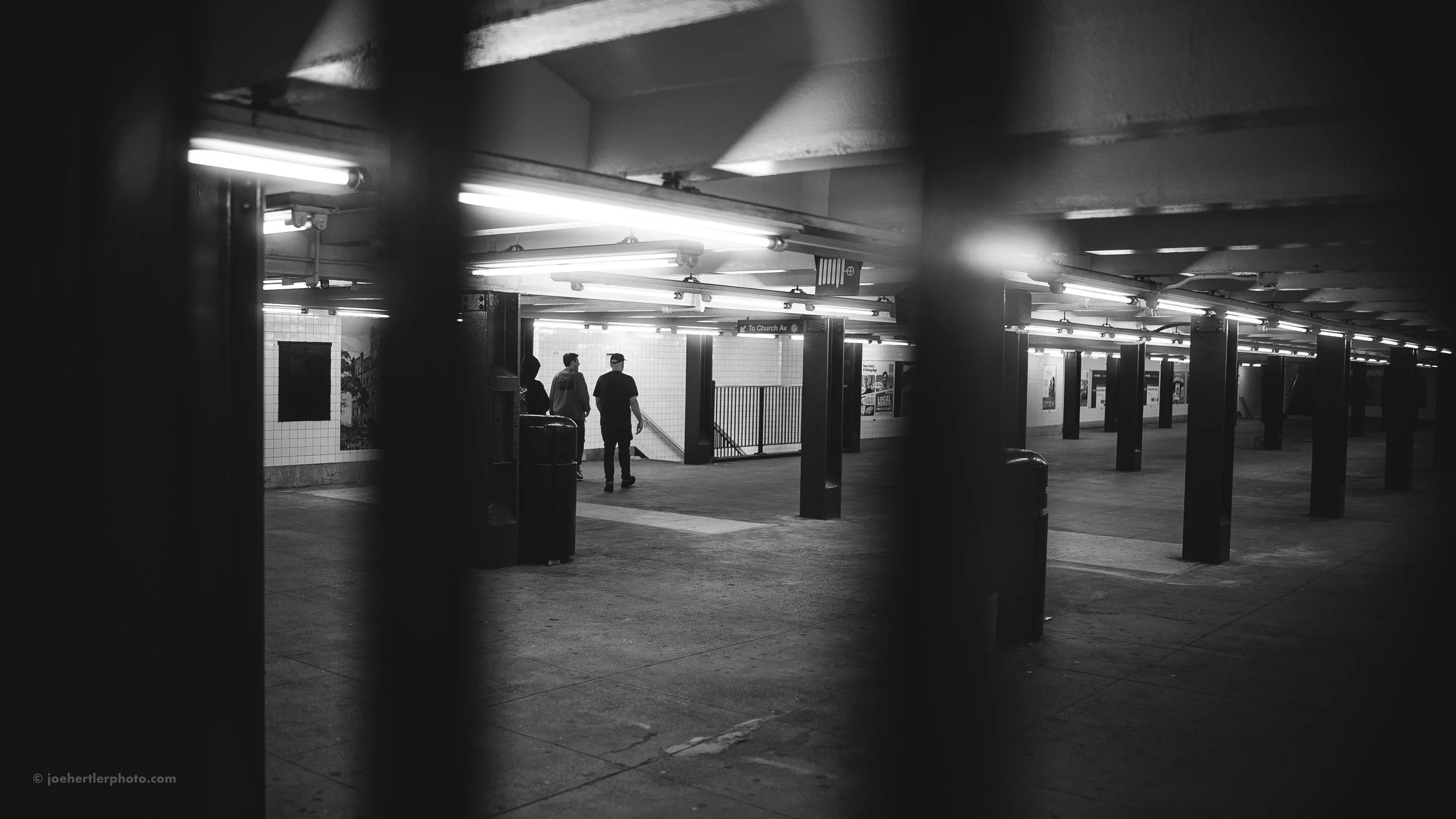 View through black bars of a dimly lit subway station with three people walking towards an exit.