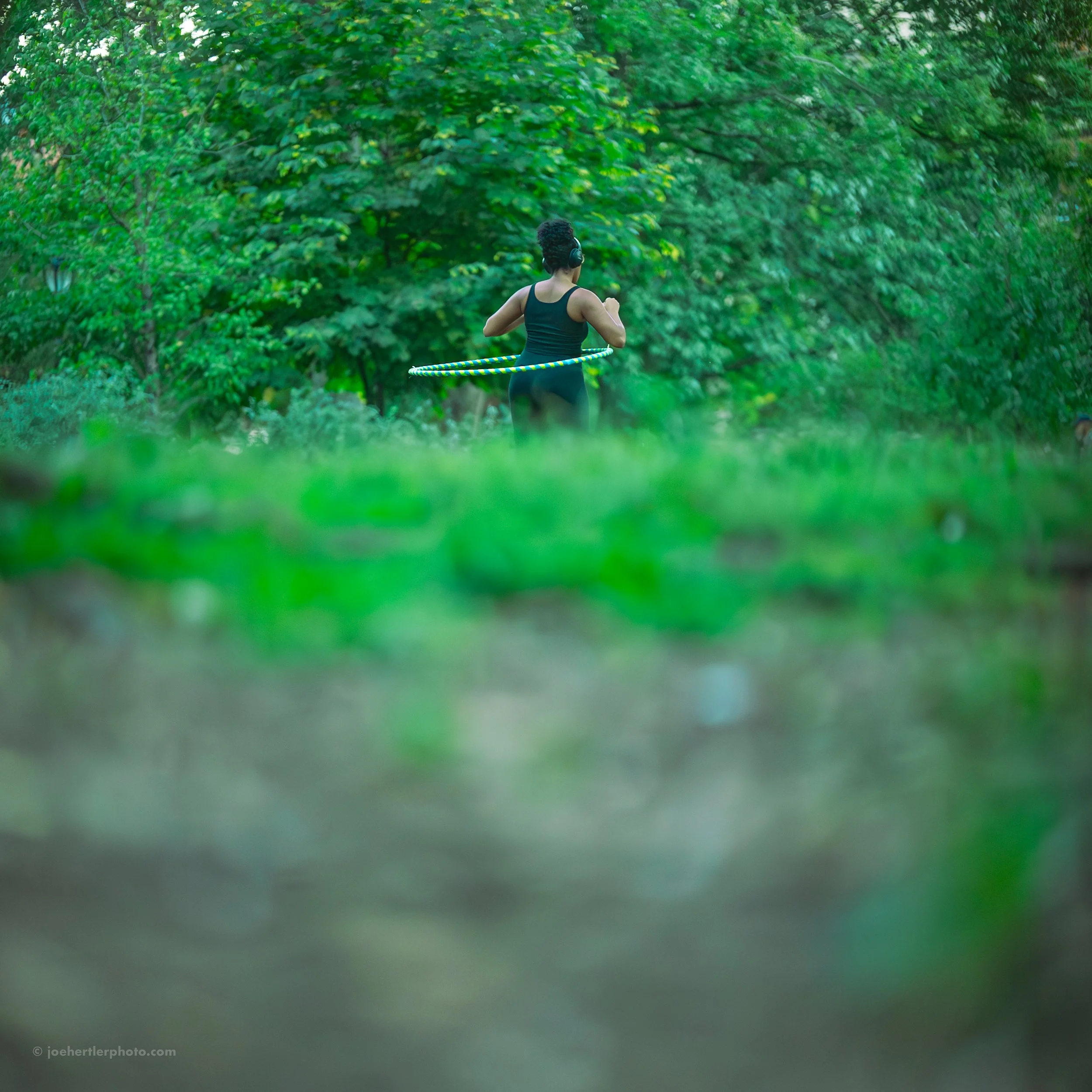 Woman in black workout clothes using a hula hoop in a lush green park.