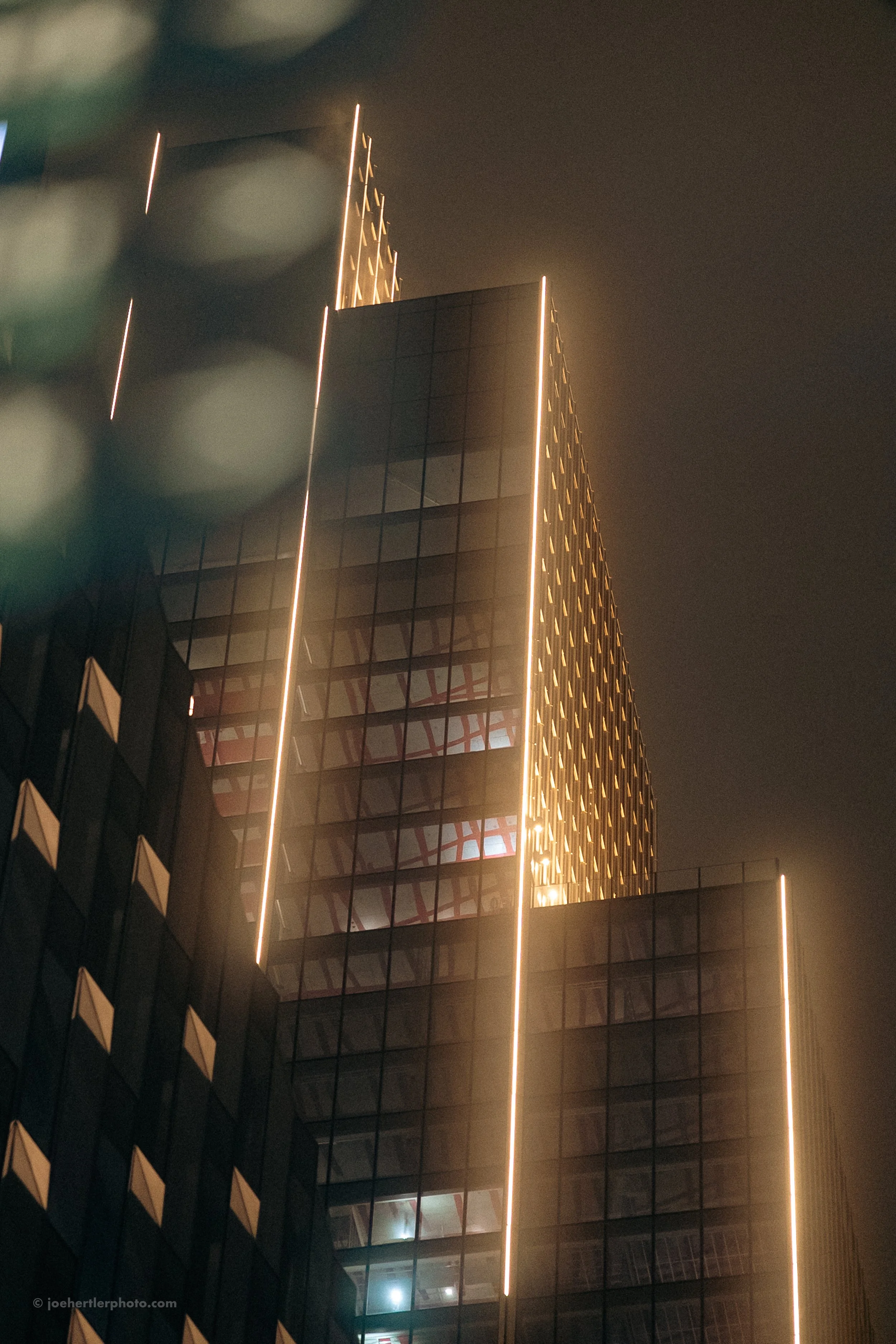 Nighttime photo of a modern glass skyscraper with illuminated vertical lines along its edges.