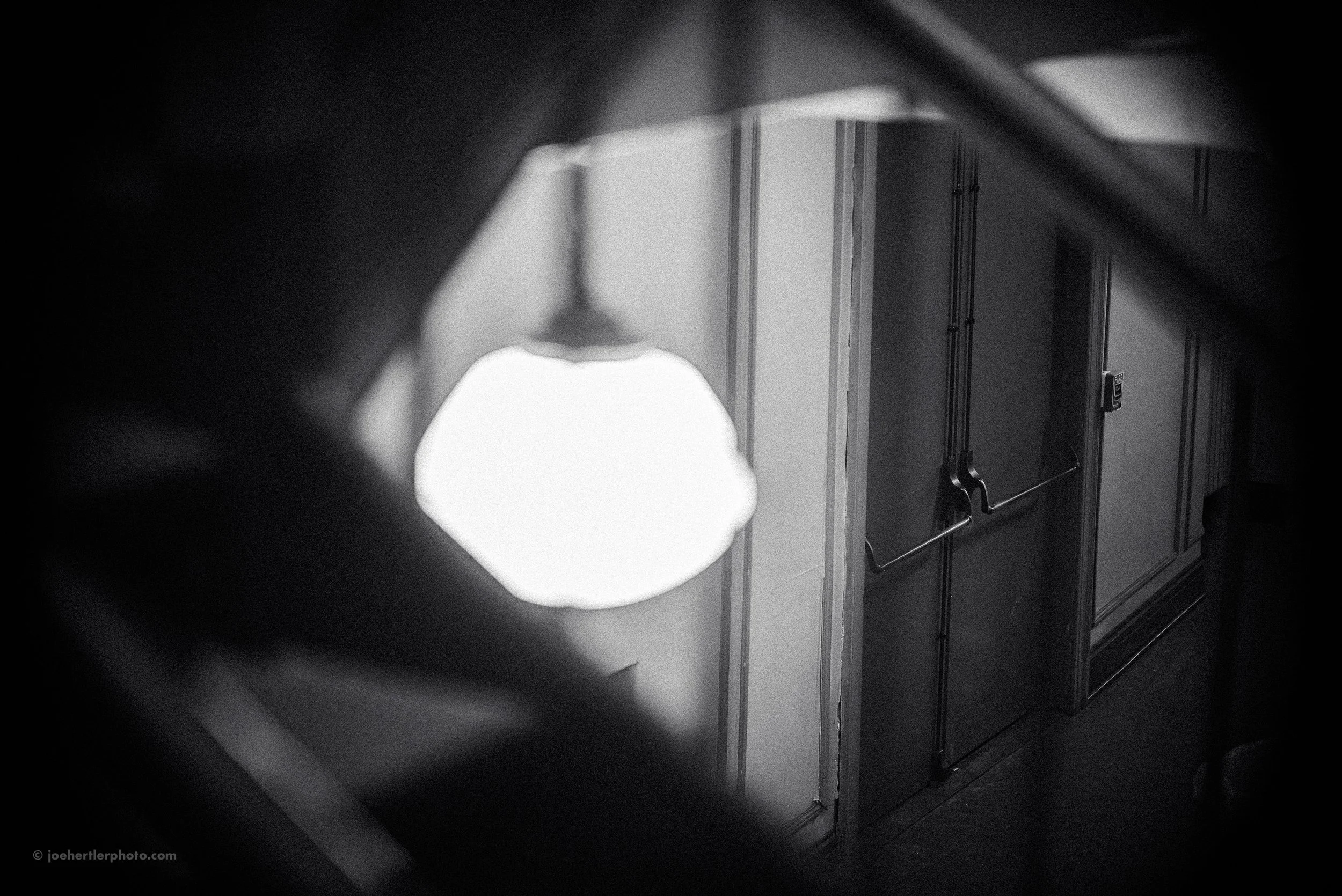 Black and white photo of a hallway with a closed door and an illuminated ceiling light fixture.