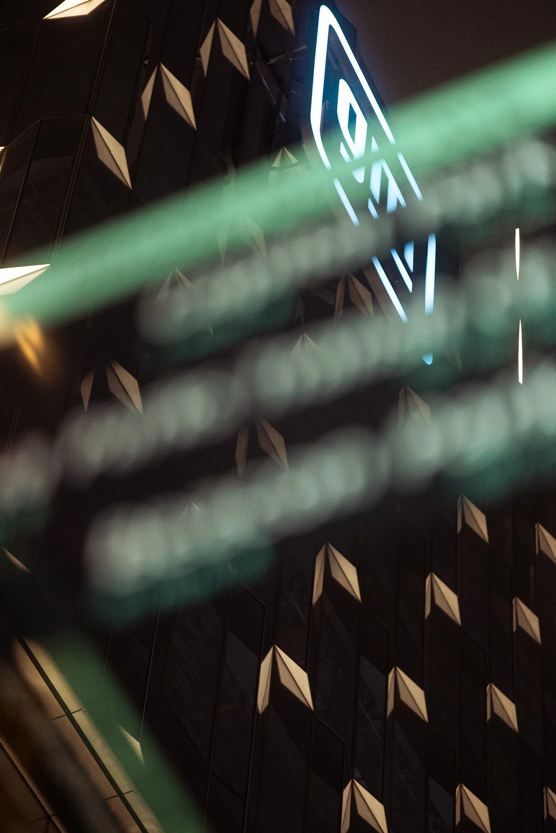 Close-up of a modern building with a patterned black exterior and illuminated signage in neon blue, partially obscured by glass railings.