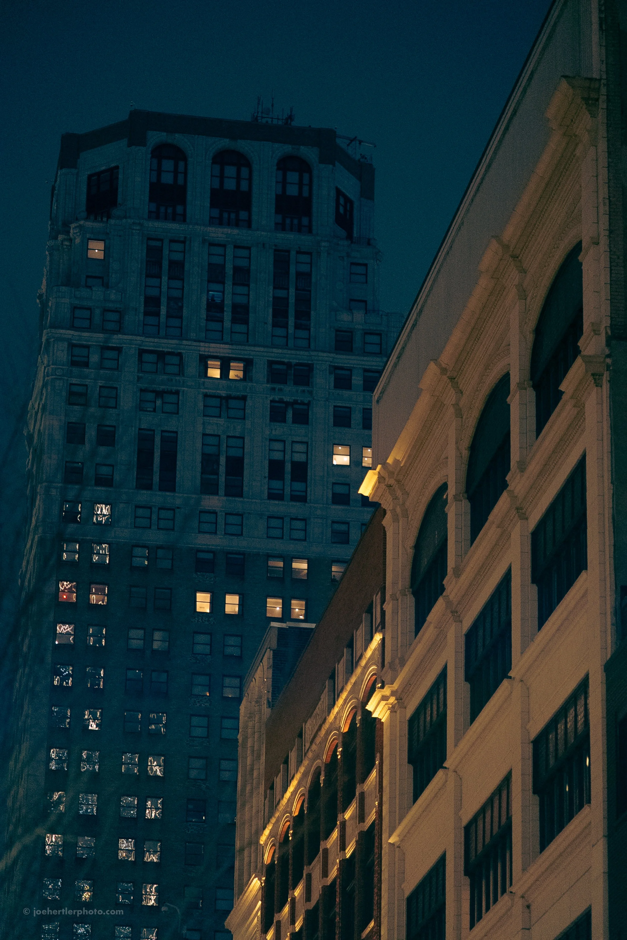 Night view of city buildings with illuminated windows and architectural details.