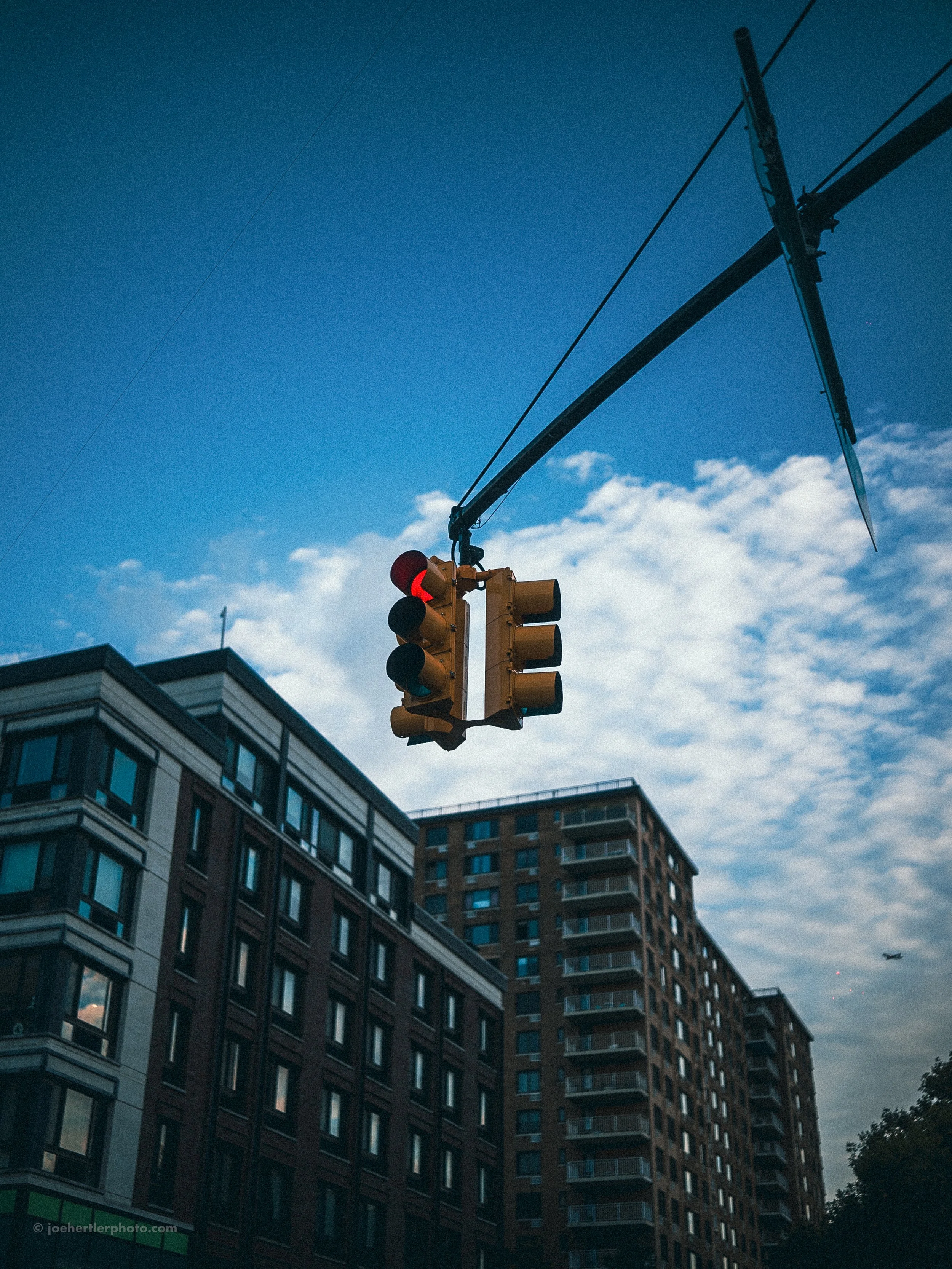 Traffic light hanging from a pole above city buildings with a blue sky and scattered clouds.