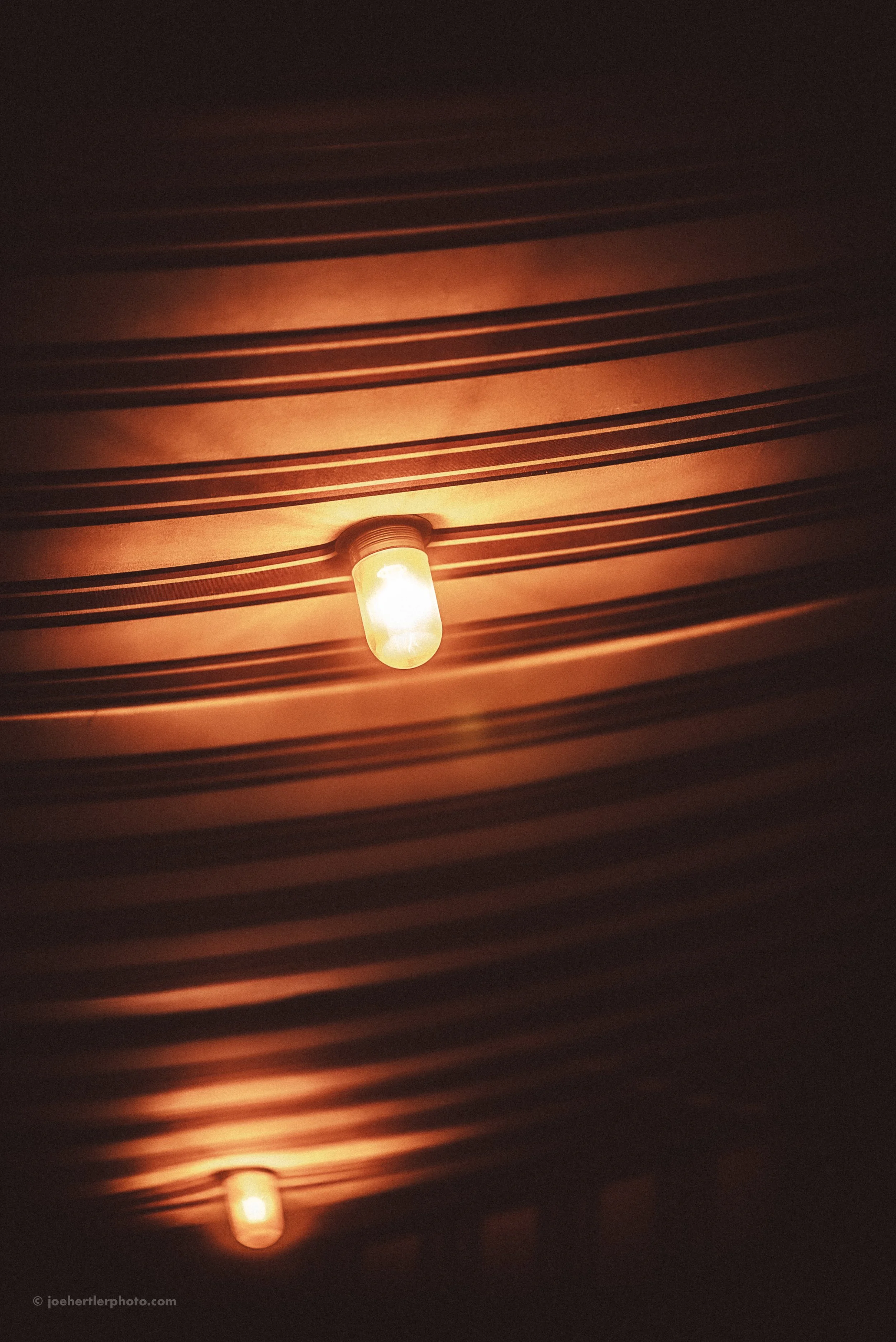 Two illuminated light bulbs on a dark ceiling with dented and scuffed surface.