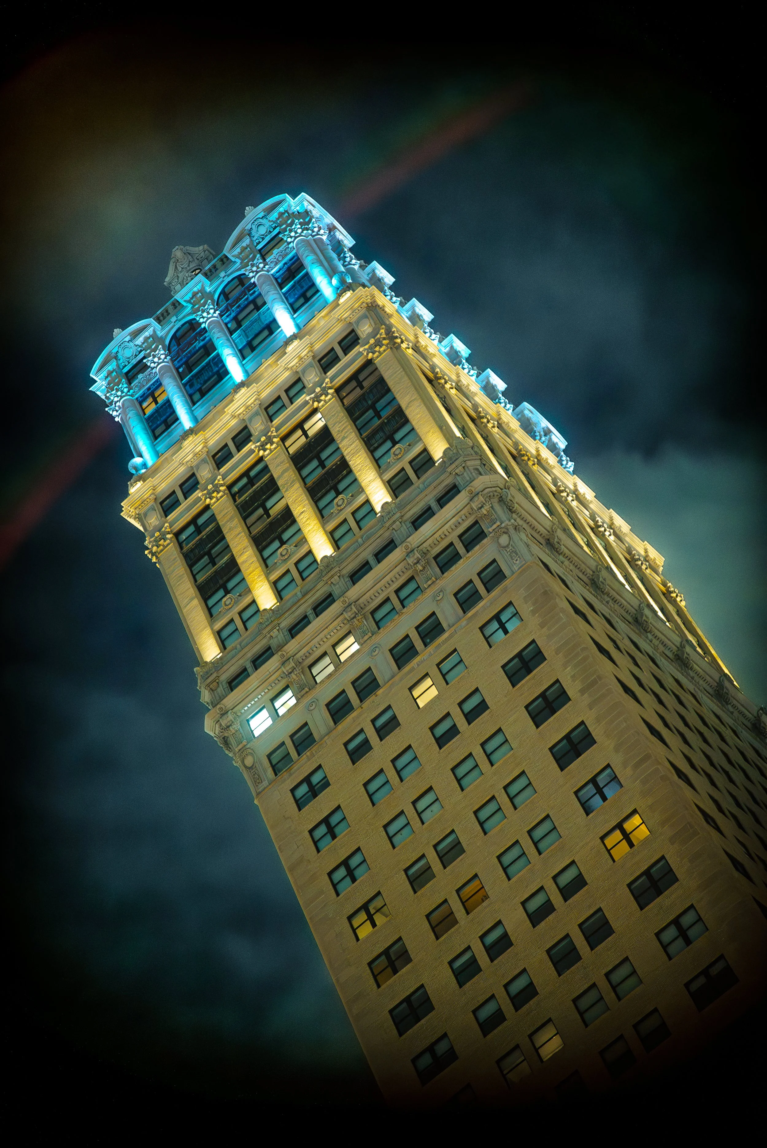 Tall illuminated building at night with a mix of yellow and blue lighting, viewed from below.