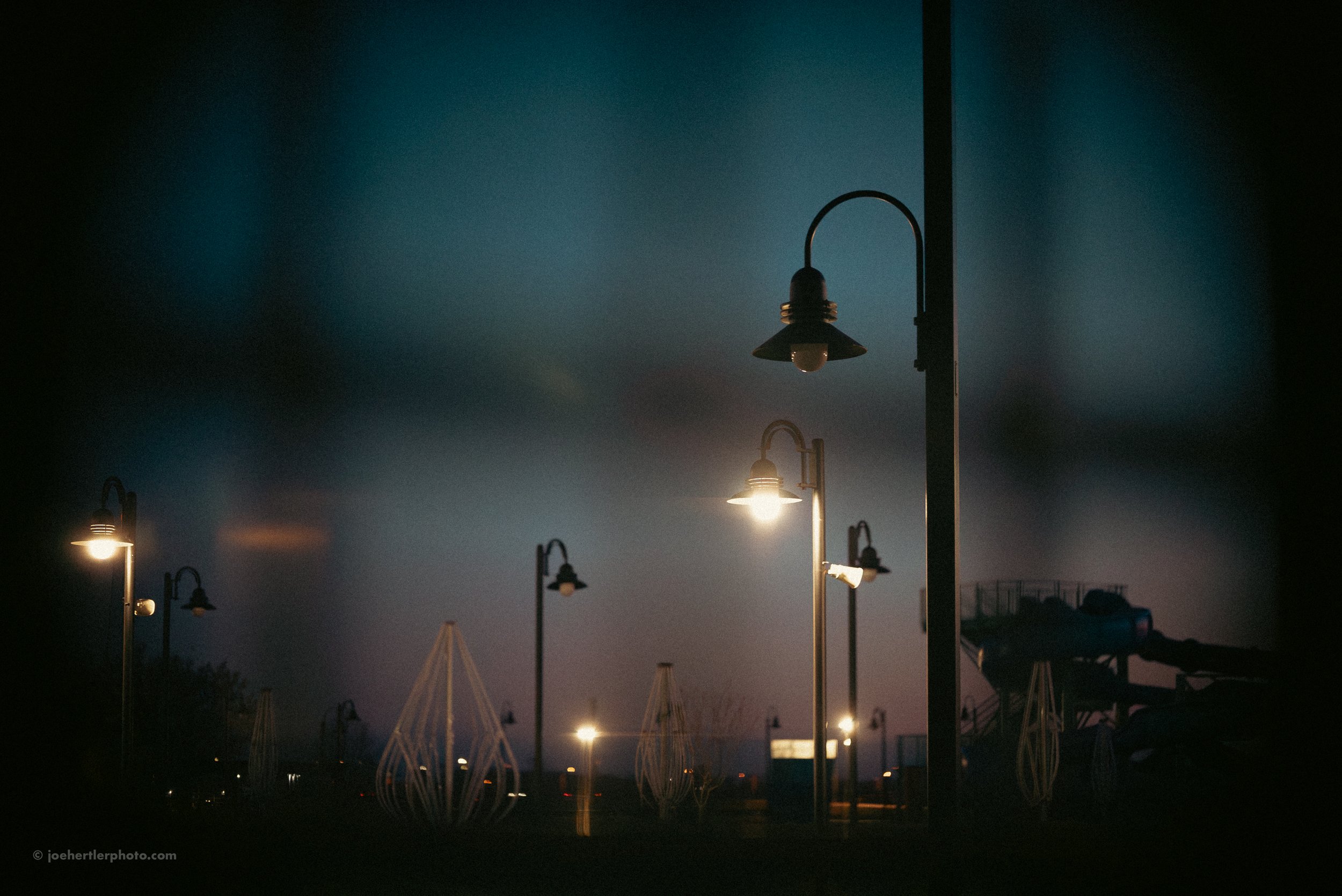 Streetlights illuminated during twilight at an empty outdoor park or recreational area.