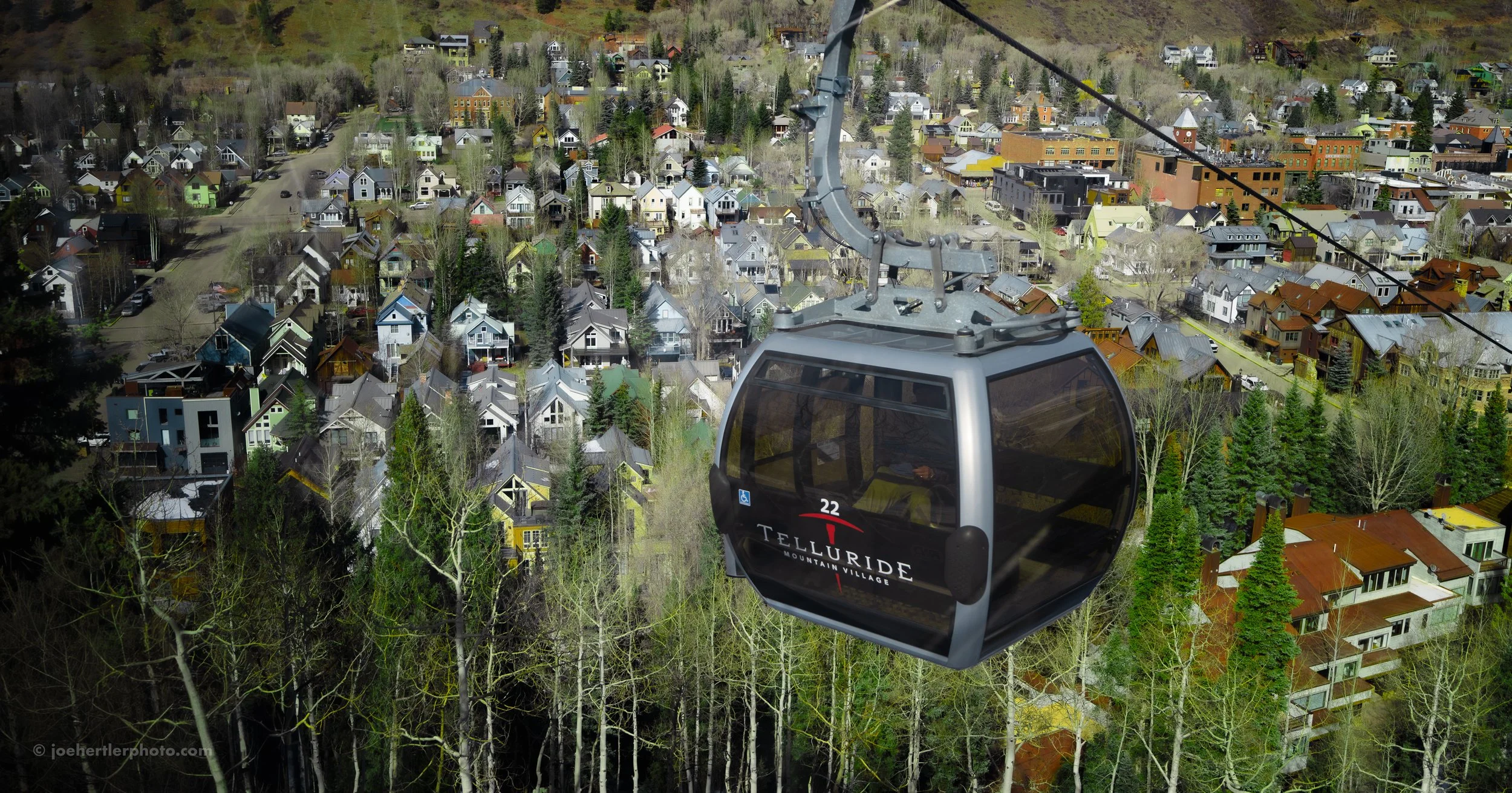 A mountain village gondola lift carrying passengers over a residential area with colorful houses and green trees in Telluride, Colorado.