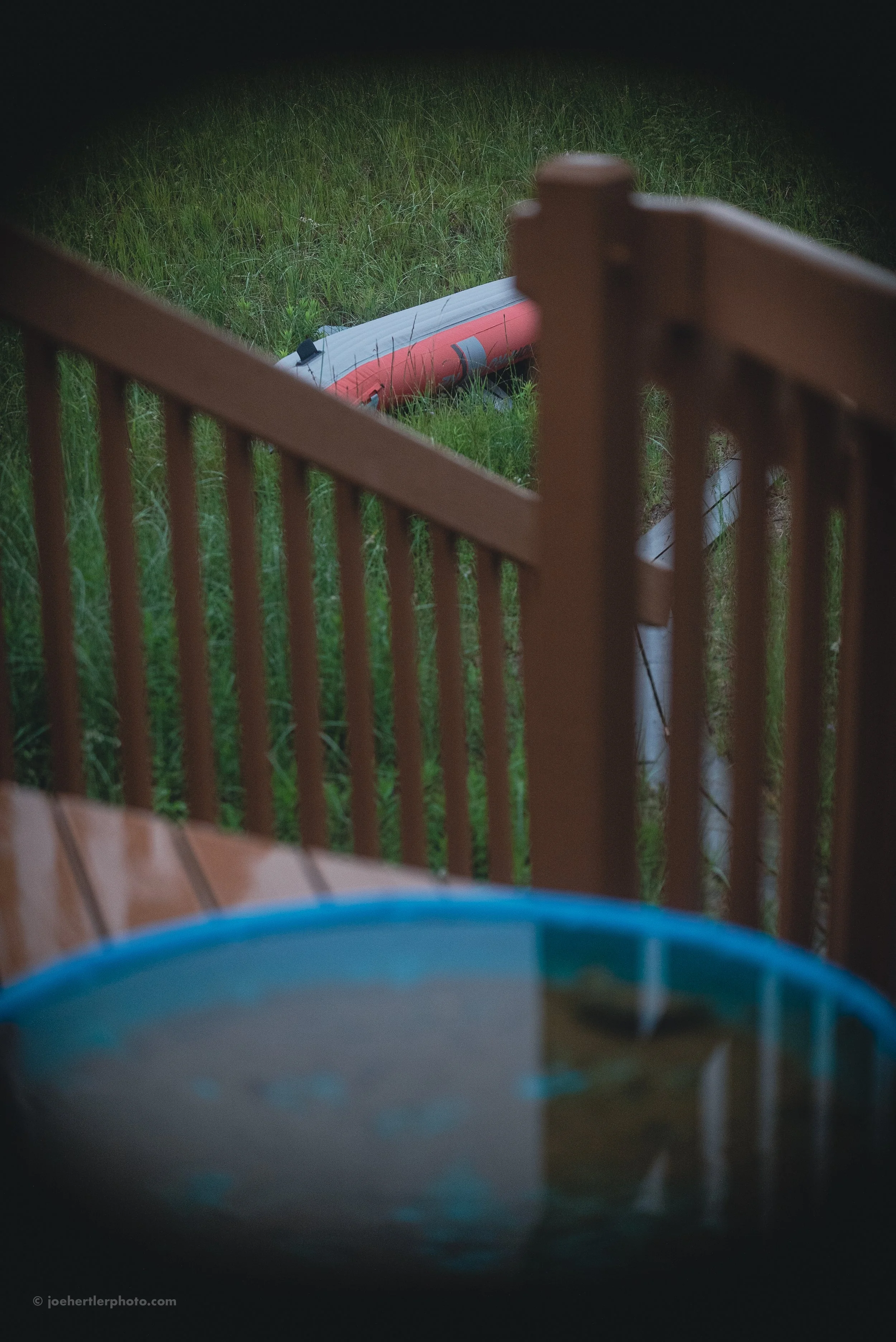 A partially visible outdoor hot tub on a wooden deck, a wooden railing, and a red kayak lying on the grass beyond the deck.