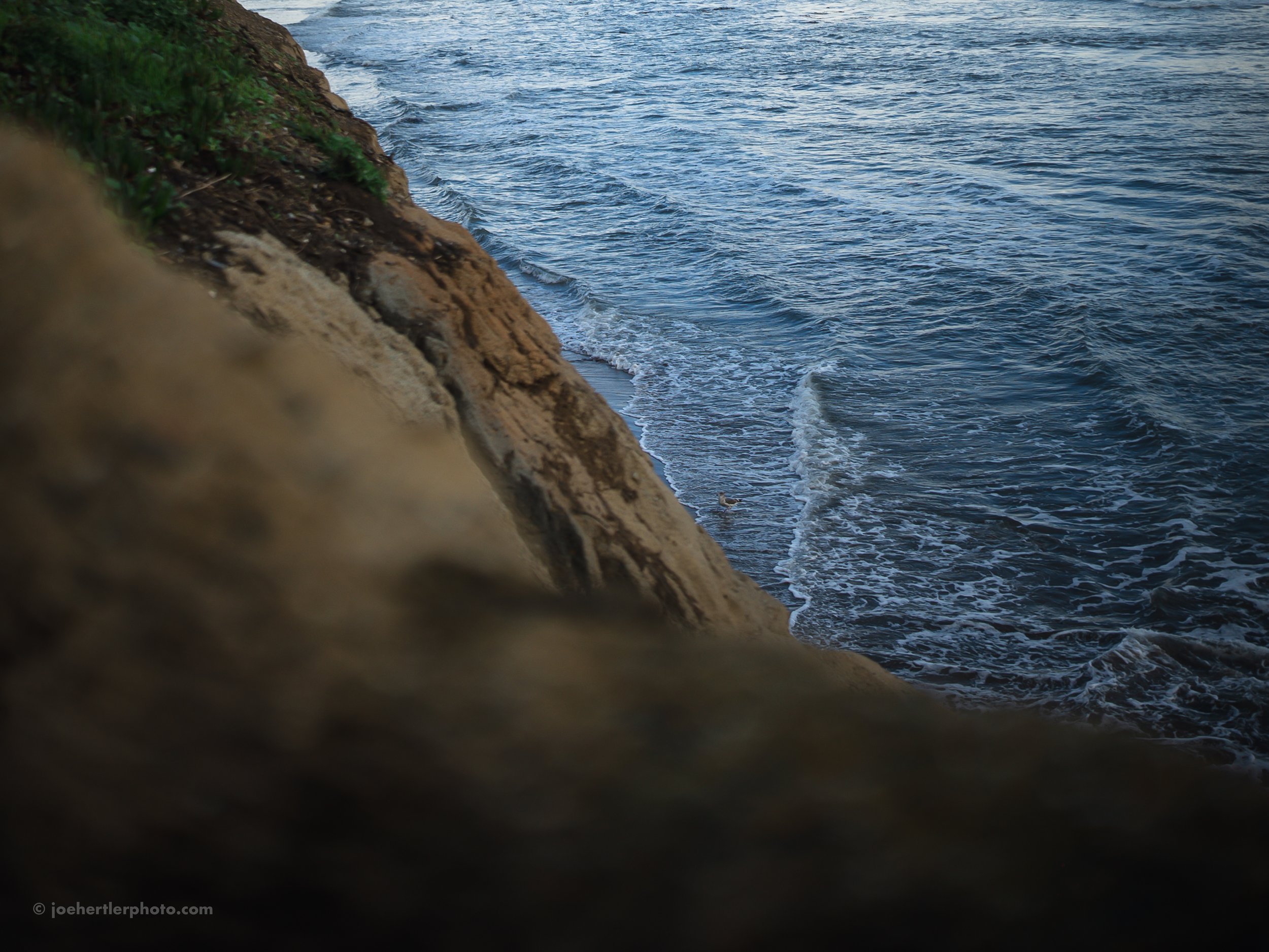 Close-up of a rocky cliffside overlooking a blue ocean with gentle waves.