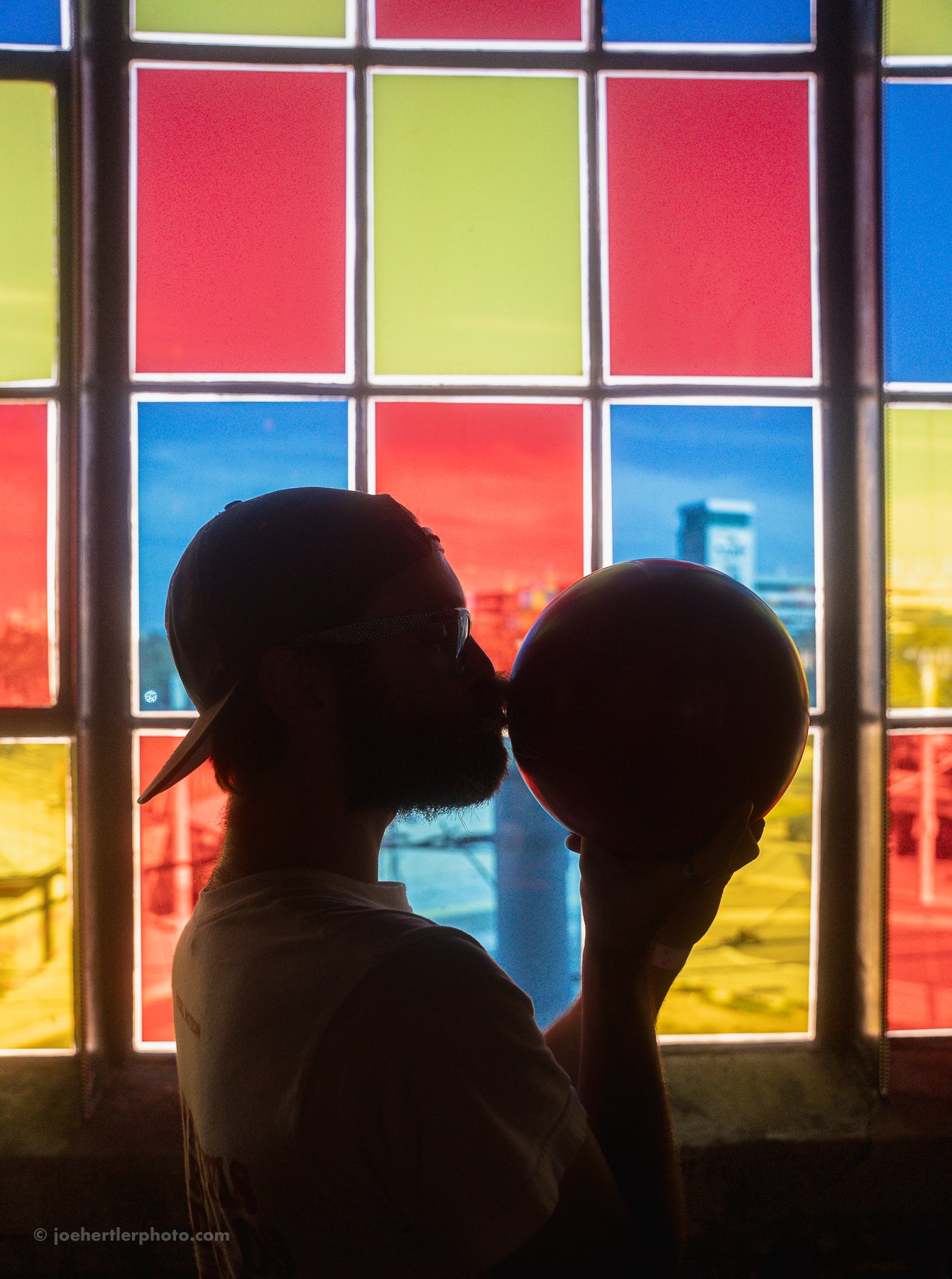 A person silhouetted in front of a colorful stained glass window, holding a ball close to their face, with the exercise of blowing into it.