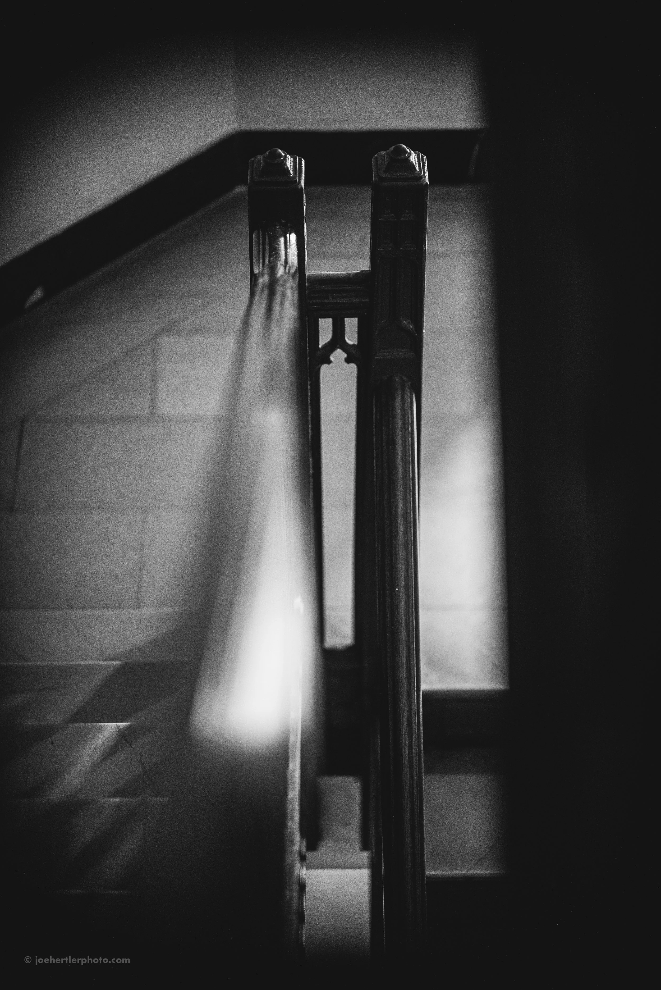 Black and white photo of a staircase viewed from above, with a handrail running down the center and steps on either side.