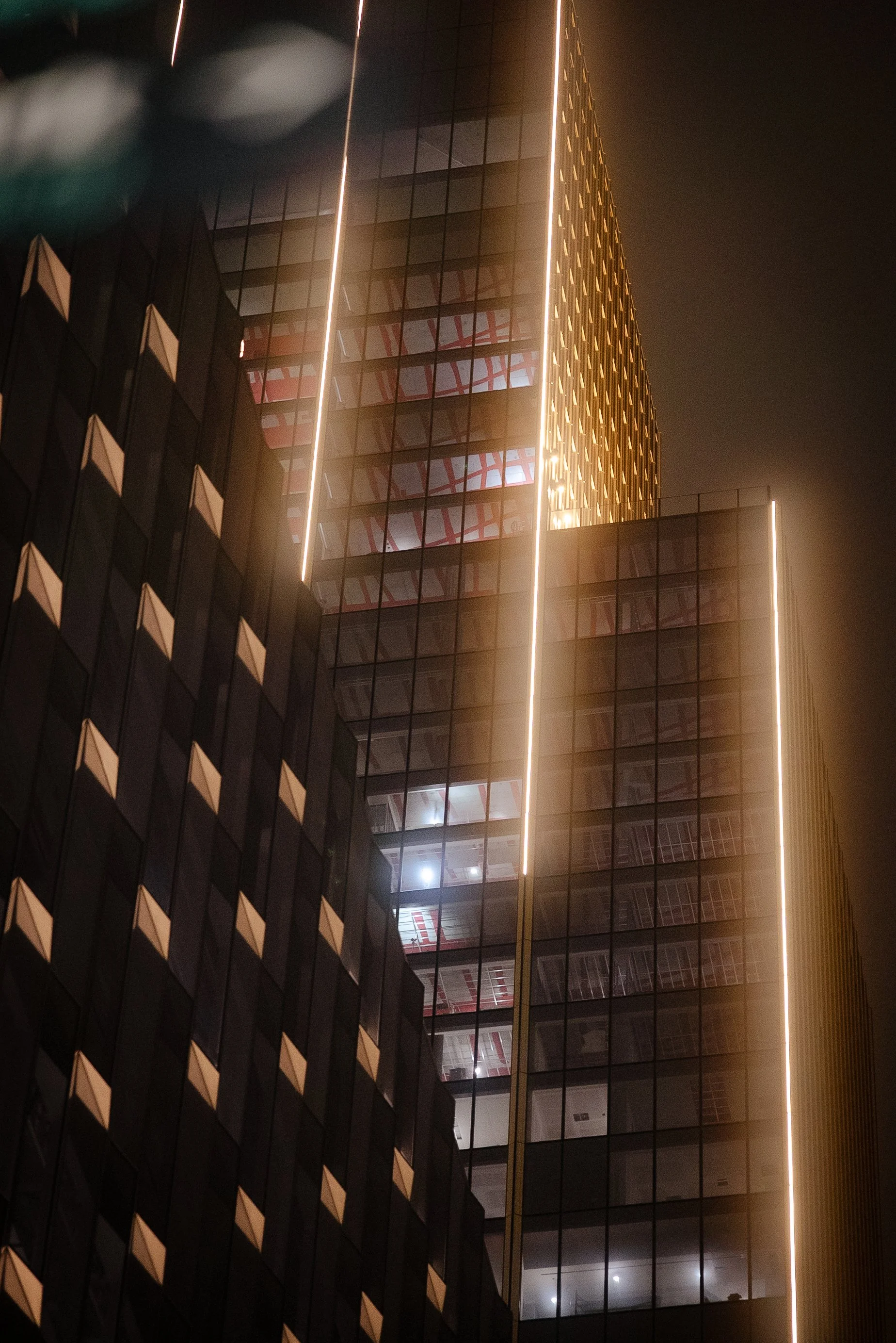 Nighttime photo of a tall modern building with glass windows and illuminated edges.