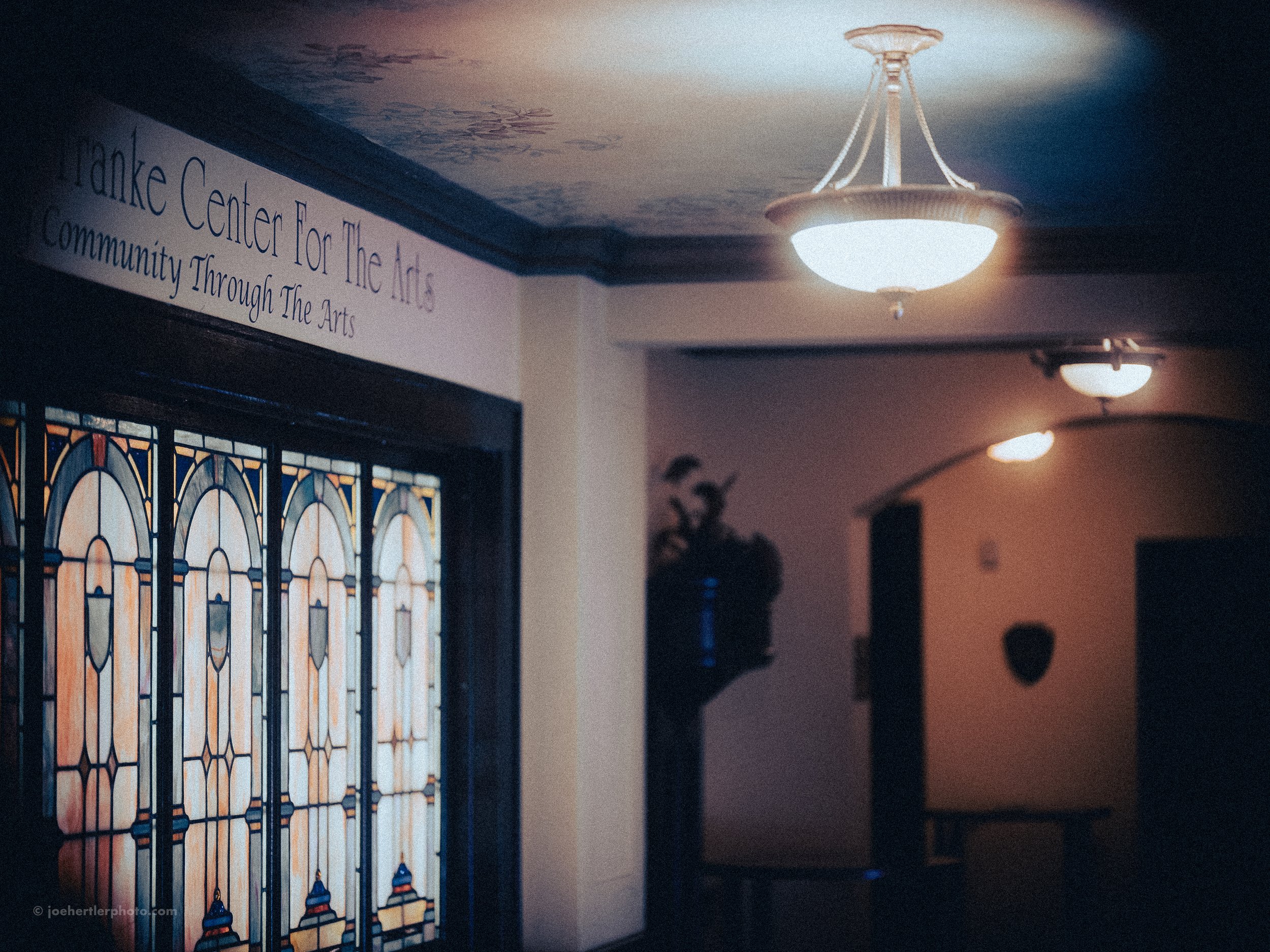 Interior of the Franke Center for the Arts with stained glass windows, dim lighting, and a sign indicating its focus on community through the arts.
