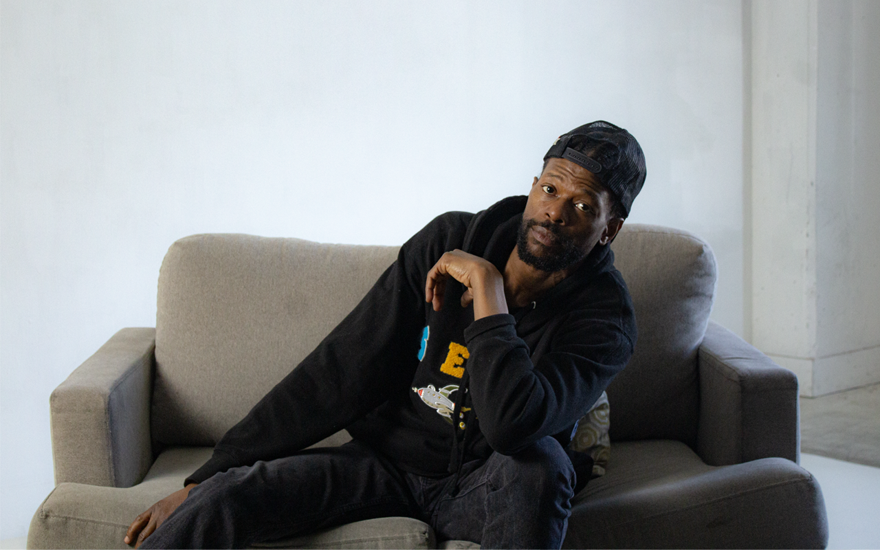 JmIsJustMe sitting on couch — West Coast progressive hip-hop, jazz rap and neo soul artist from Mid-City Los Angeles