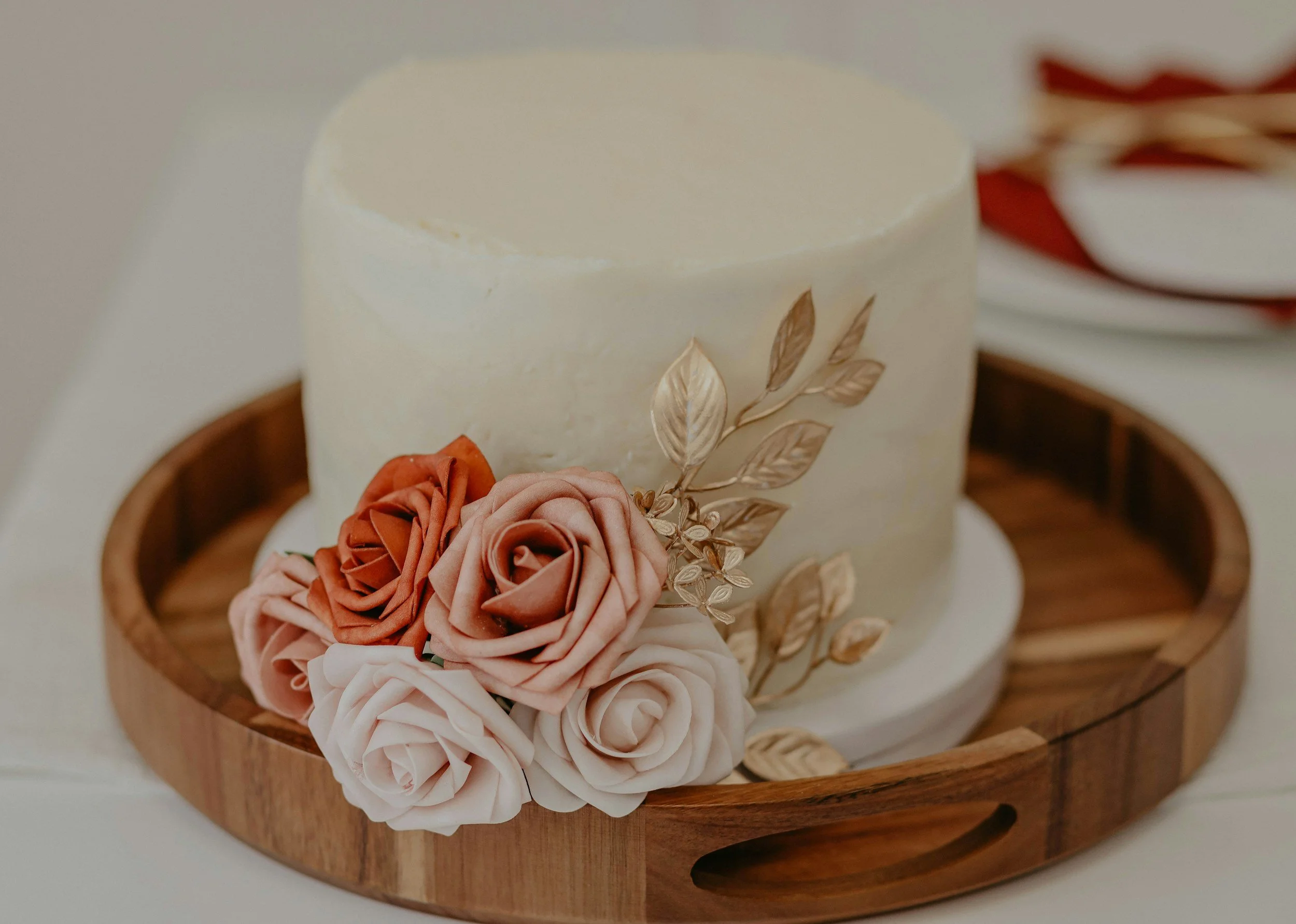 Decorative cake with floral icing and golden leaves in a wooden bowl.