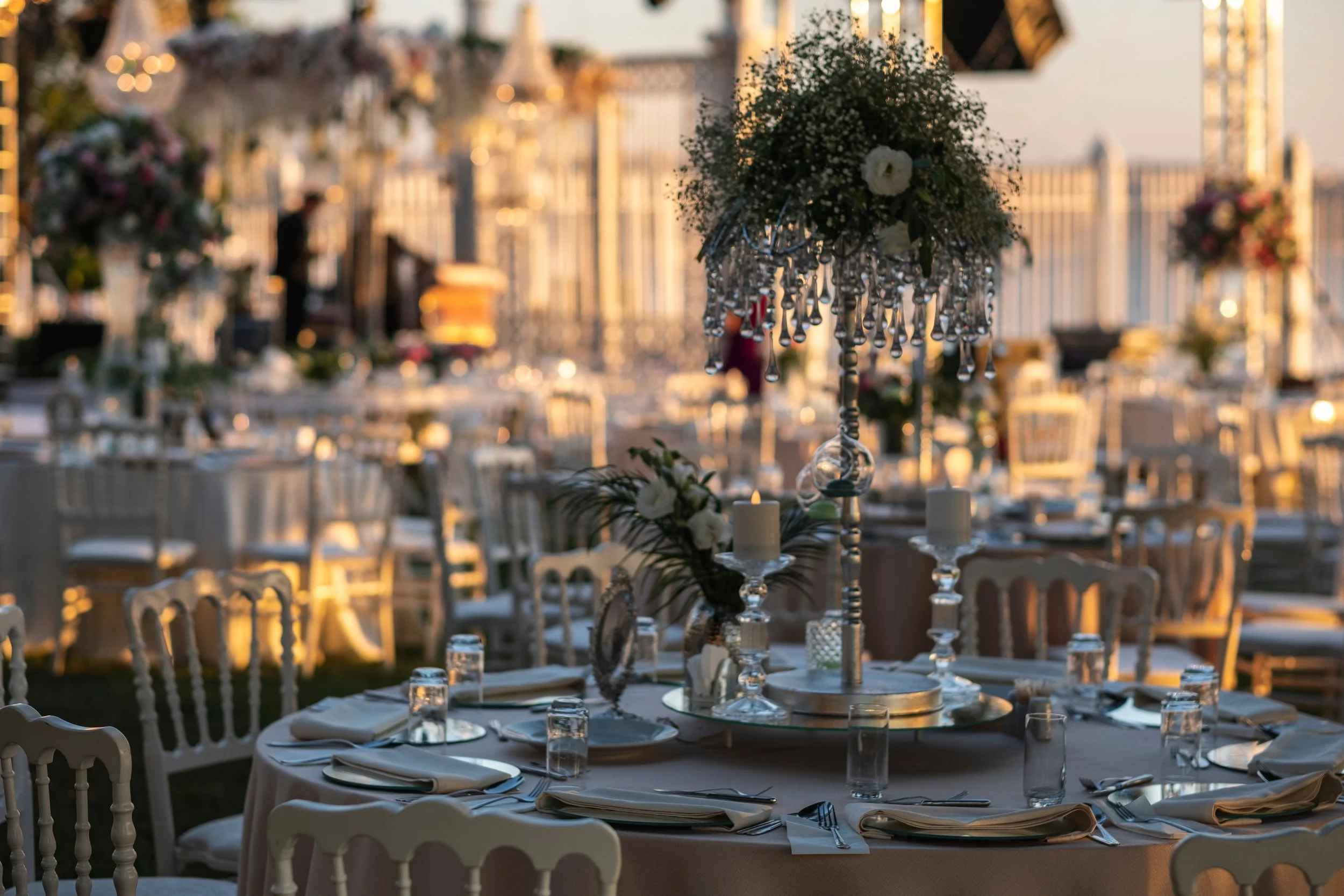Luxuriös gedeckte Hochzeitstafel bei Sonnenuntergang mit eleganter Floristik, Kerzenlicht und stilvollen Kristalldetails.