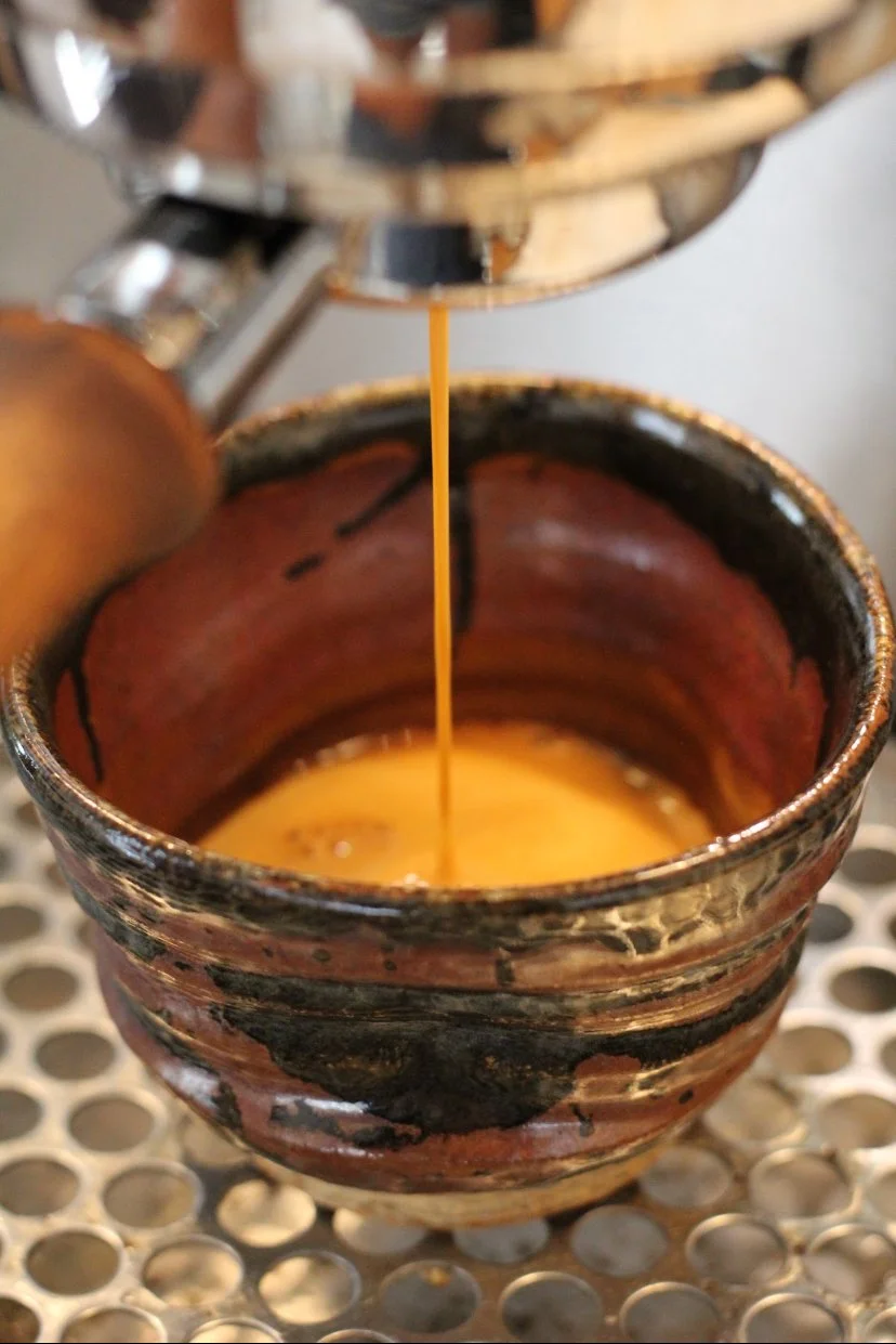 Dark brown coffee being poured from a metallic espresso machine into a rustic ceramic cup.