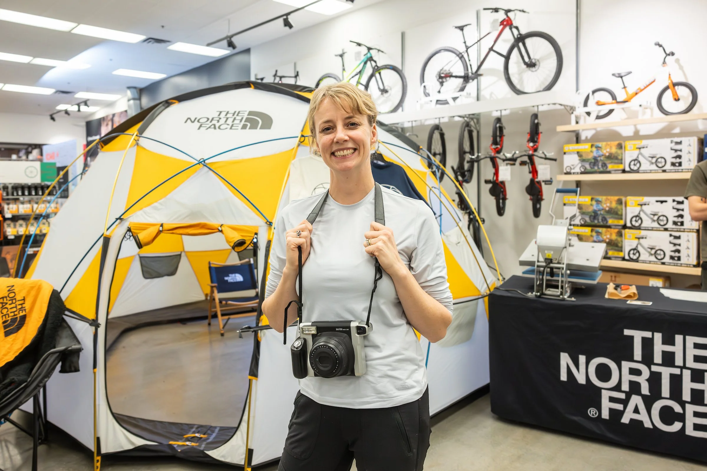 Woman inside a sporting goods store, standing in front of a yellow tent, with bicycles and bike accessories displayed on the walls behind her.