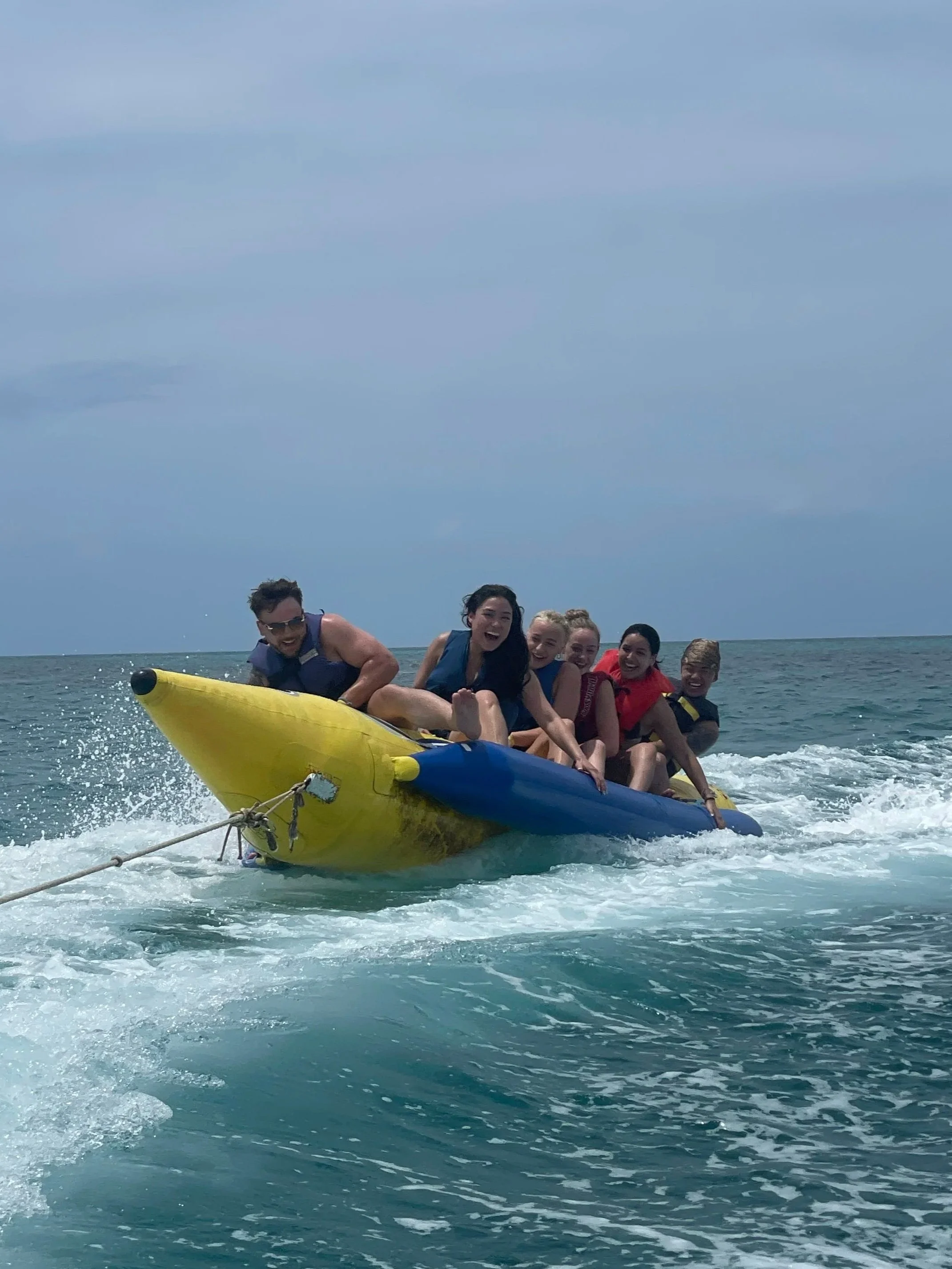 Six friends riding a banana boat on the beaches clear water all screaming as the banana boat is about to tilt on its side