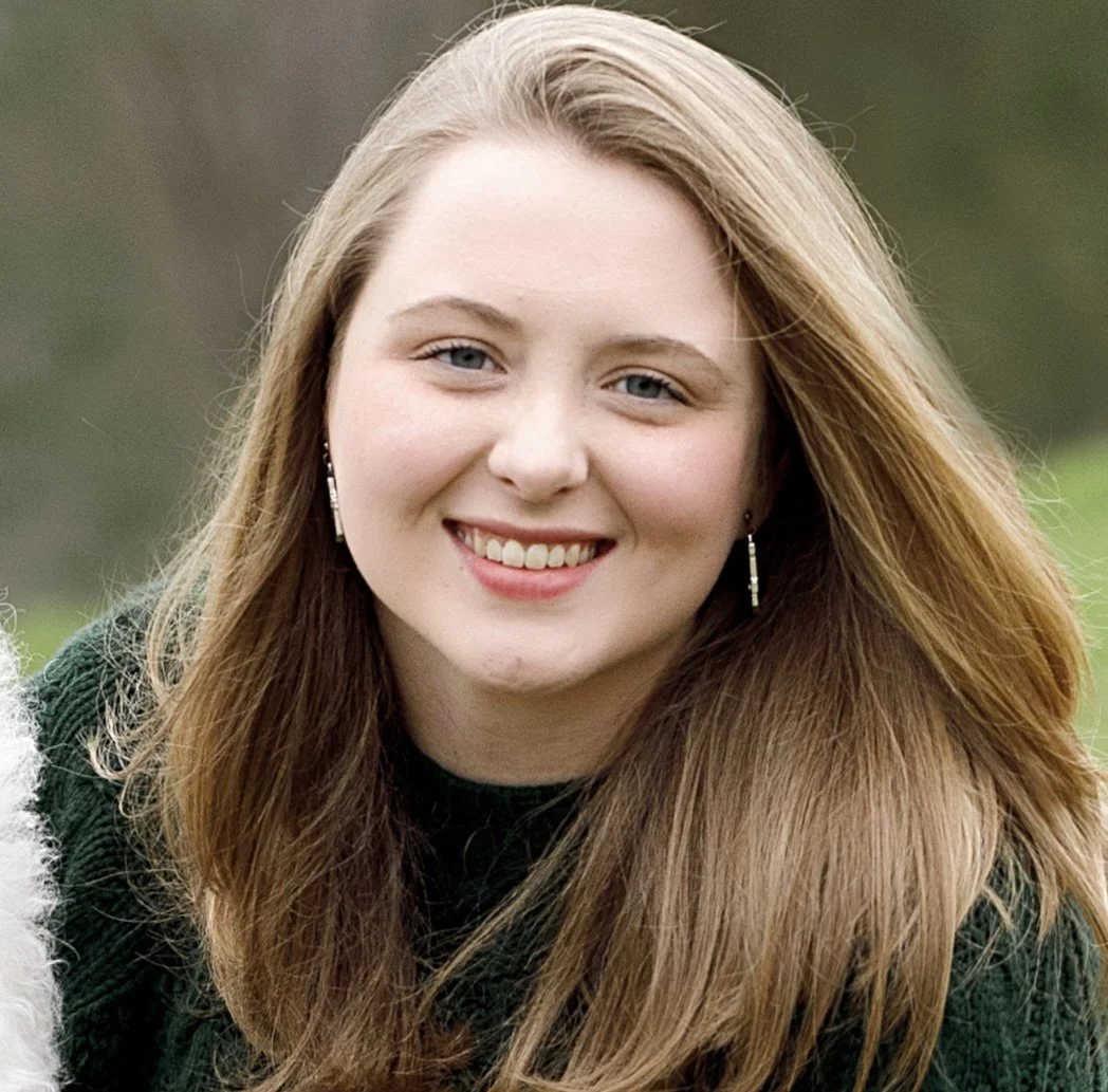 A young woman (Kelley LeCroy) with long, light blonde hair, blue eyes, and wearing earrings, smiling outdoors.