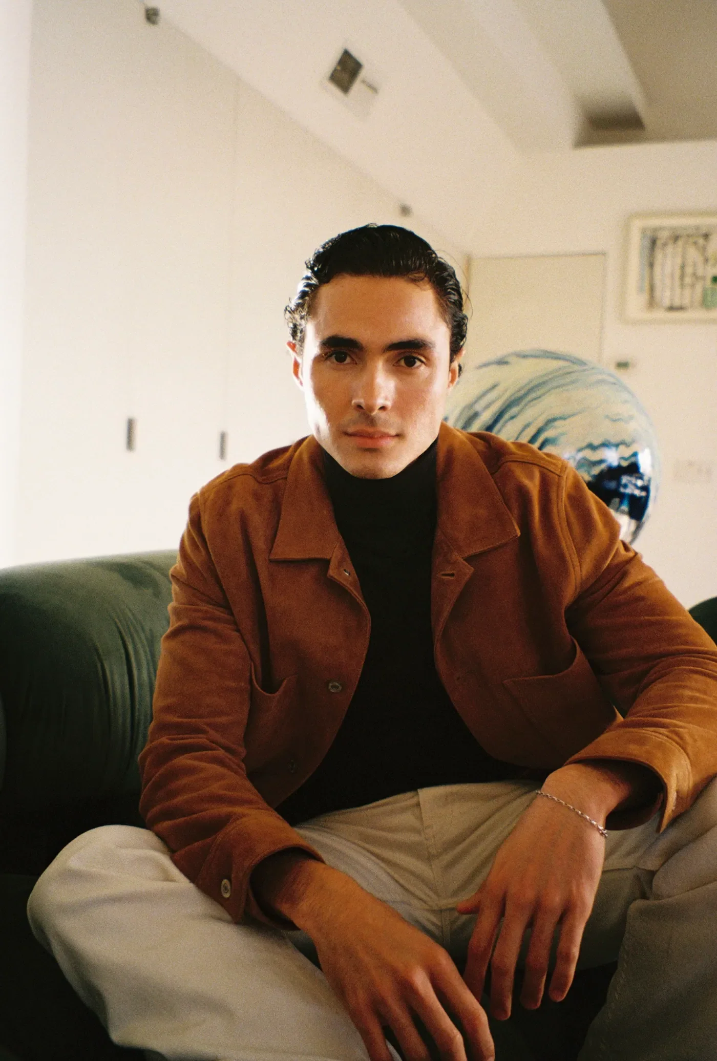 Luis del Toro actor portrait sitting wearing brown jacket and black turtleneck indoors