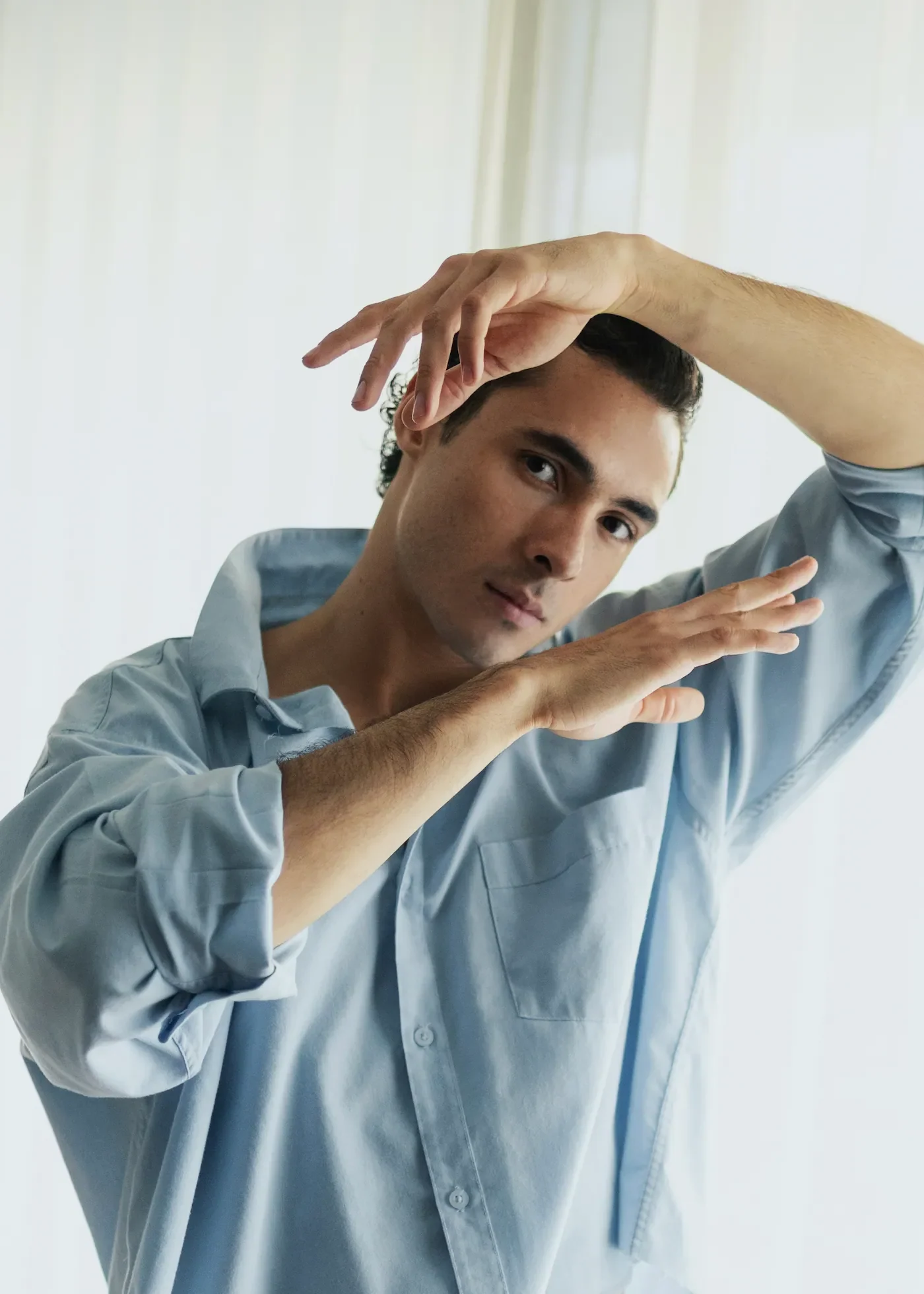 Luis del Toro actor portrait wearing blue shirt with hands framing face against white background