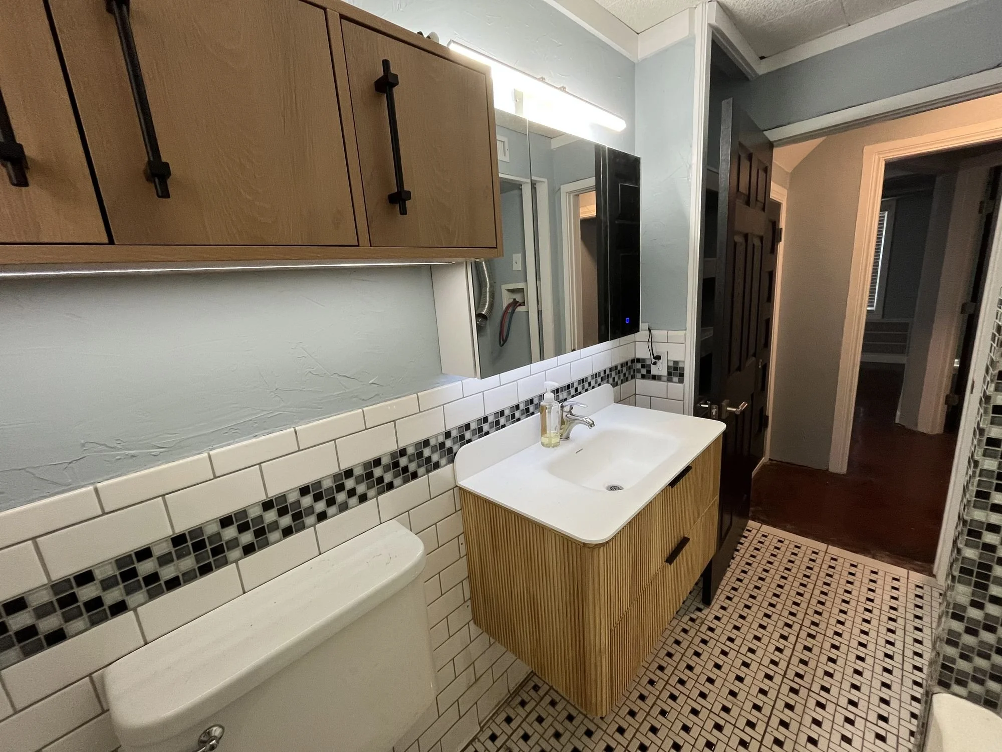 Wood-front bathroom vanity with a white basin beside existing mosaic and subway tile