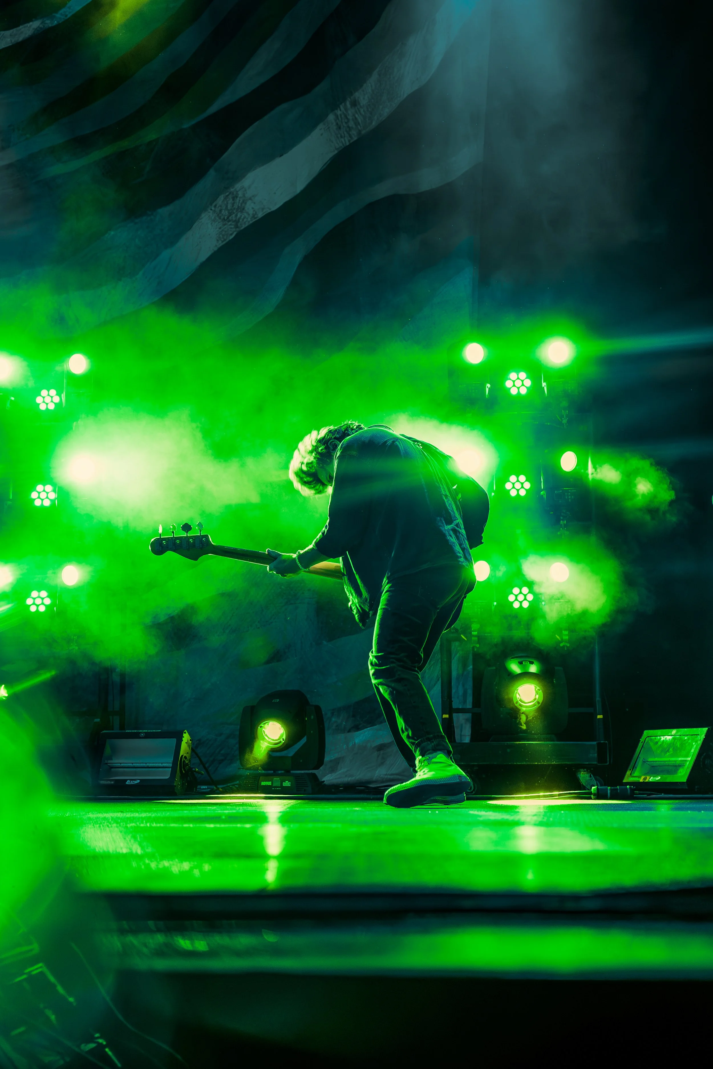 A musician playing an electric guitar on a stage illuminated with green stage lights and fog.