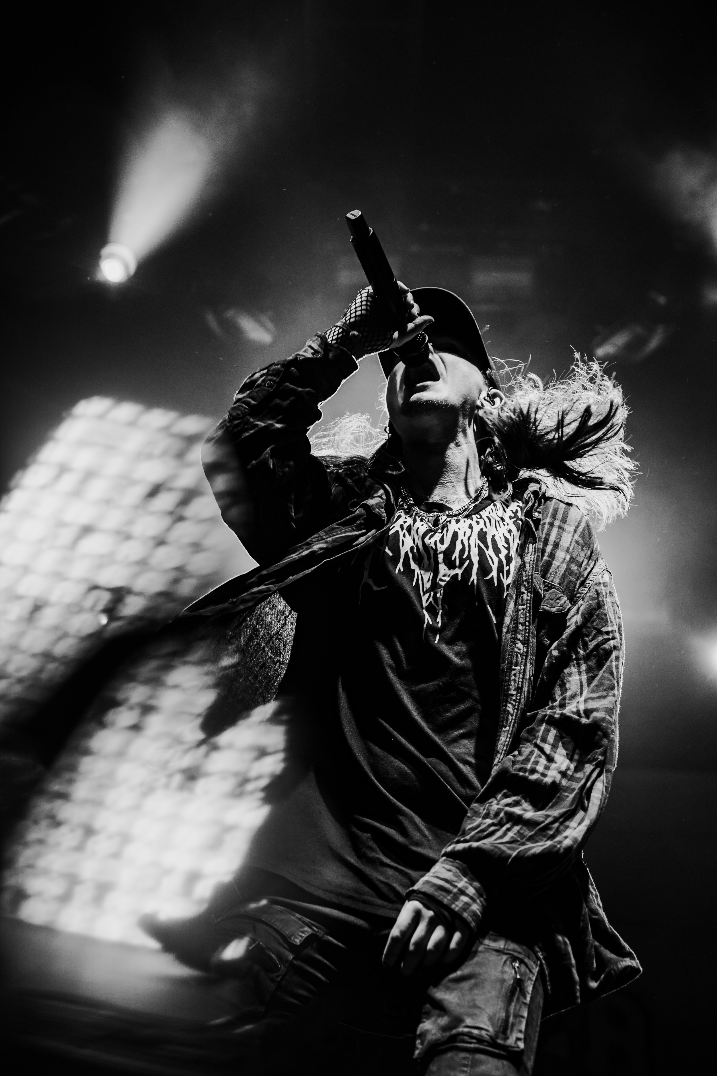 Black and white image of a singer performing on stage, holding a microphone close to their mouth, with hair flowing and illuminated by stage lights.