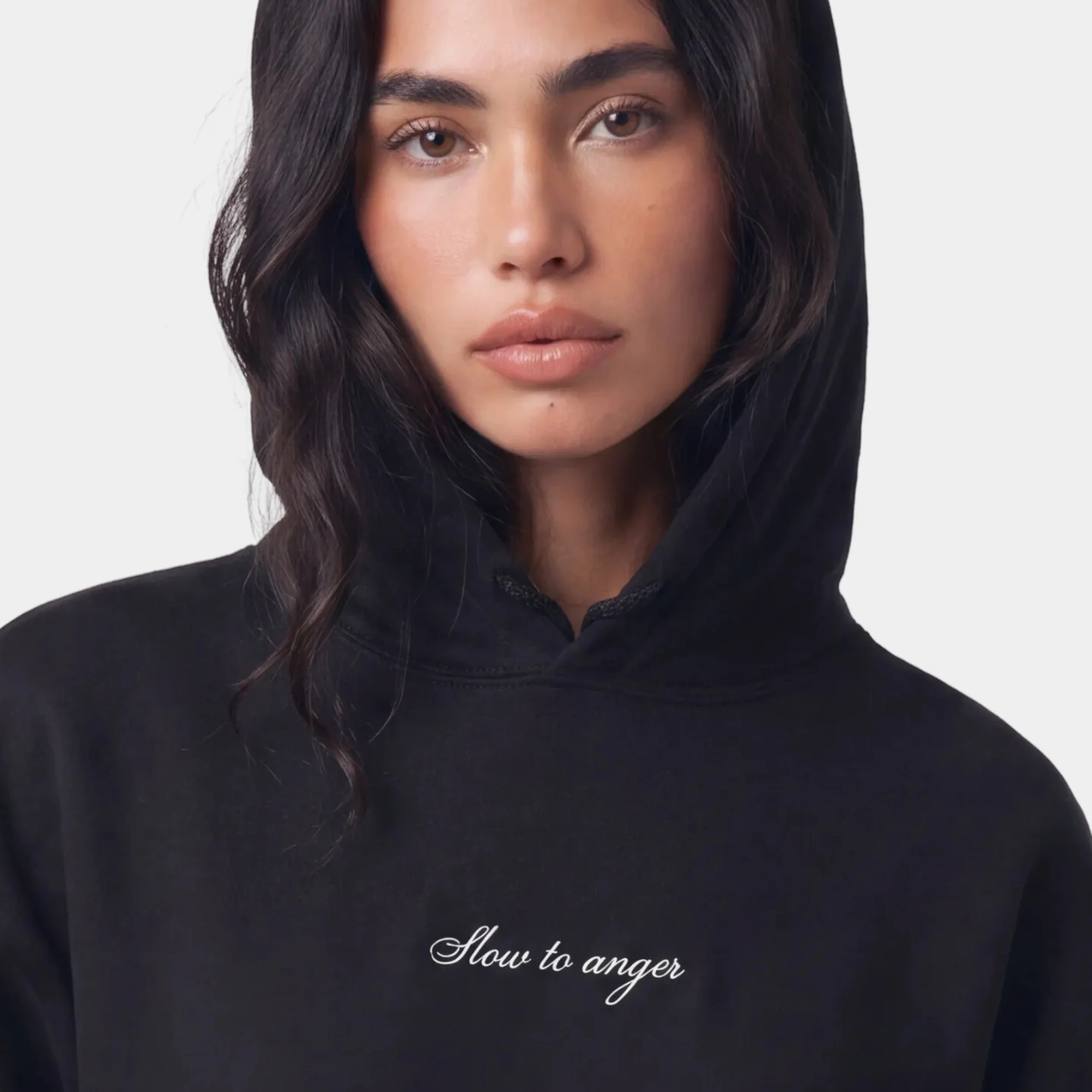 Close-up of a young woman's face with dark wavy hair and brown eyes, wearing a black top with white script