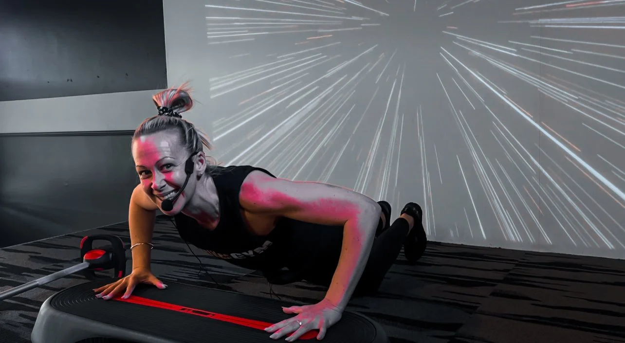 A woman in workout attire using a treadmill in a futuristic gym with a starfield projection on the wall, smiling and looking at the camera.